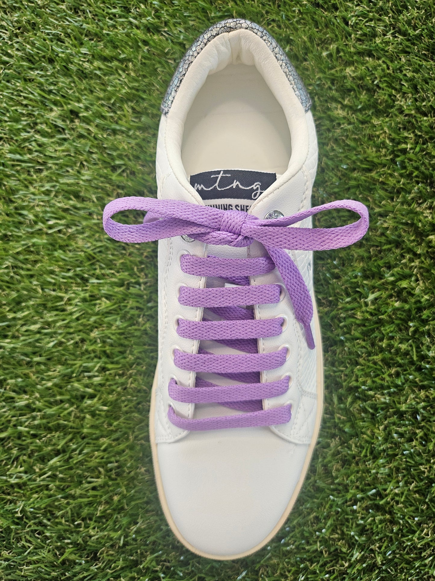 White sneaker with purple laces on a grass background