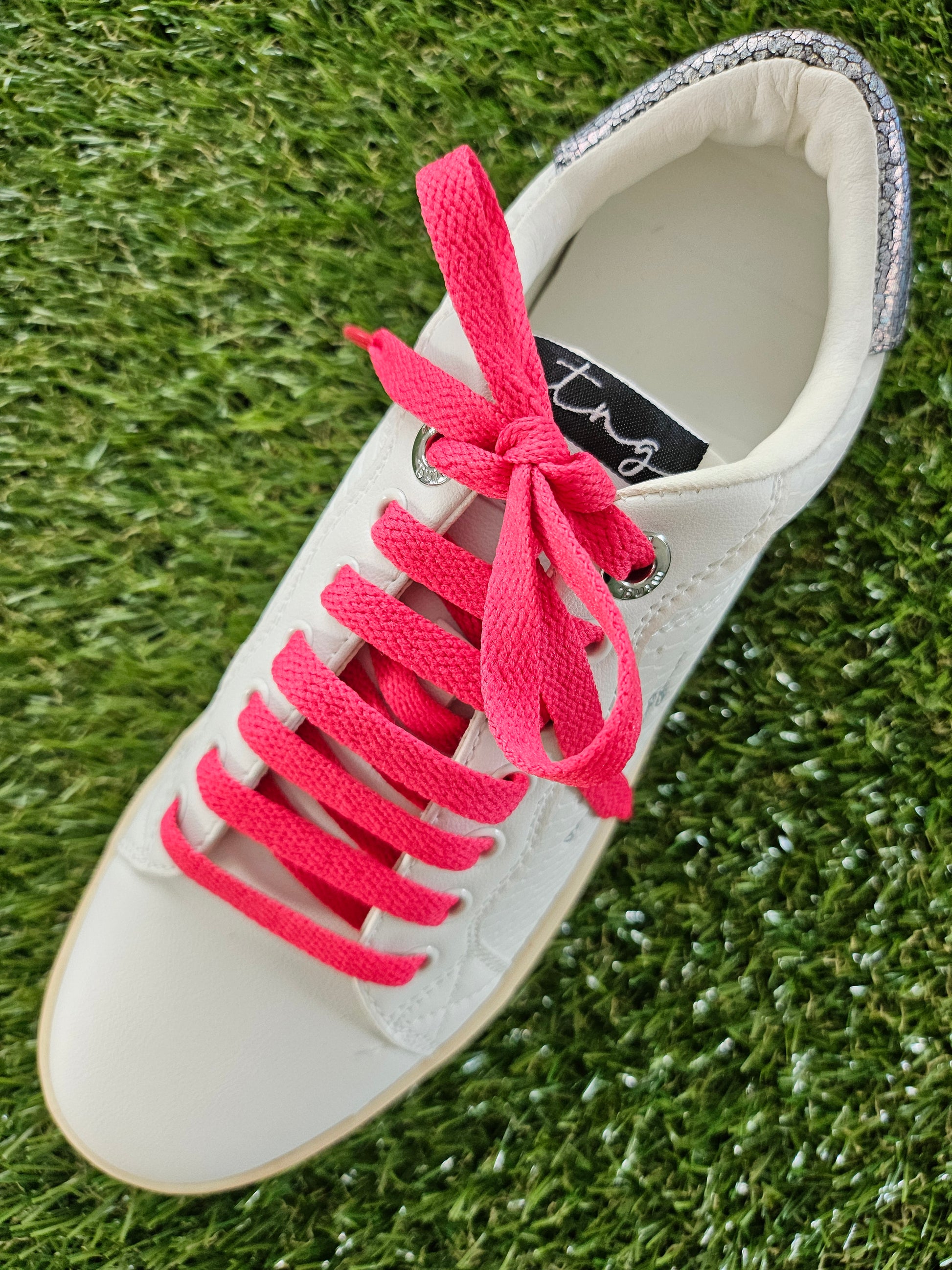 White trainer with watermelon pink laces on a grass background