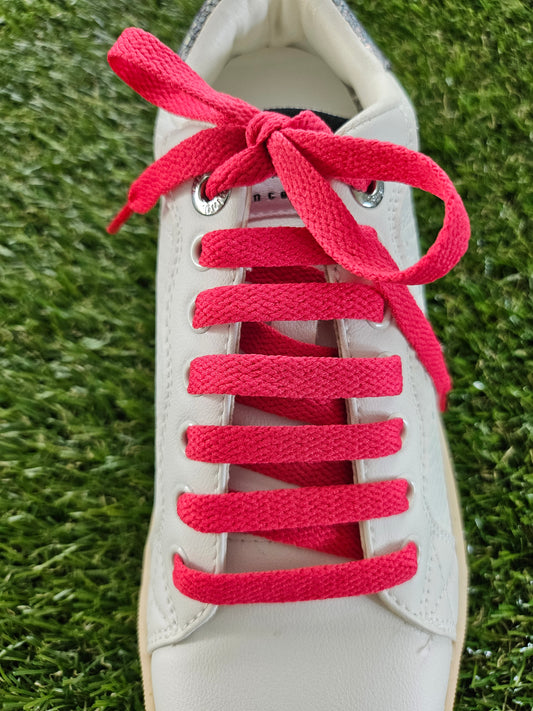 White trainer with watermelon red laces on a grass background