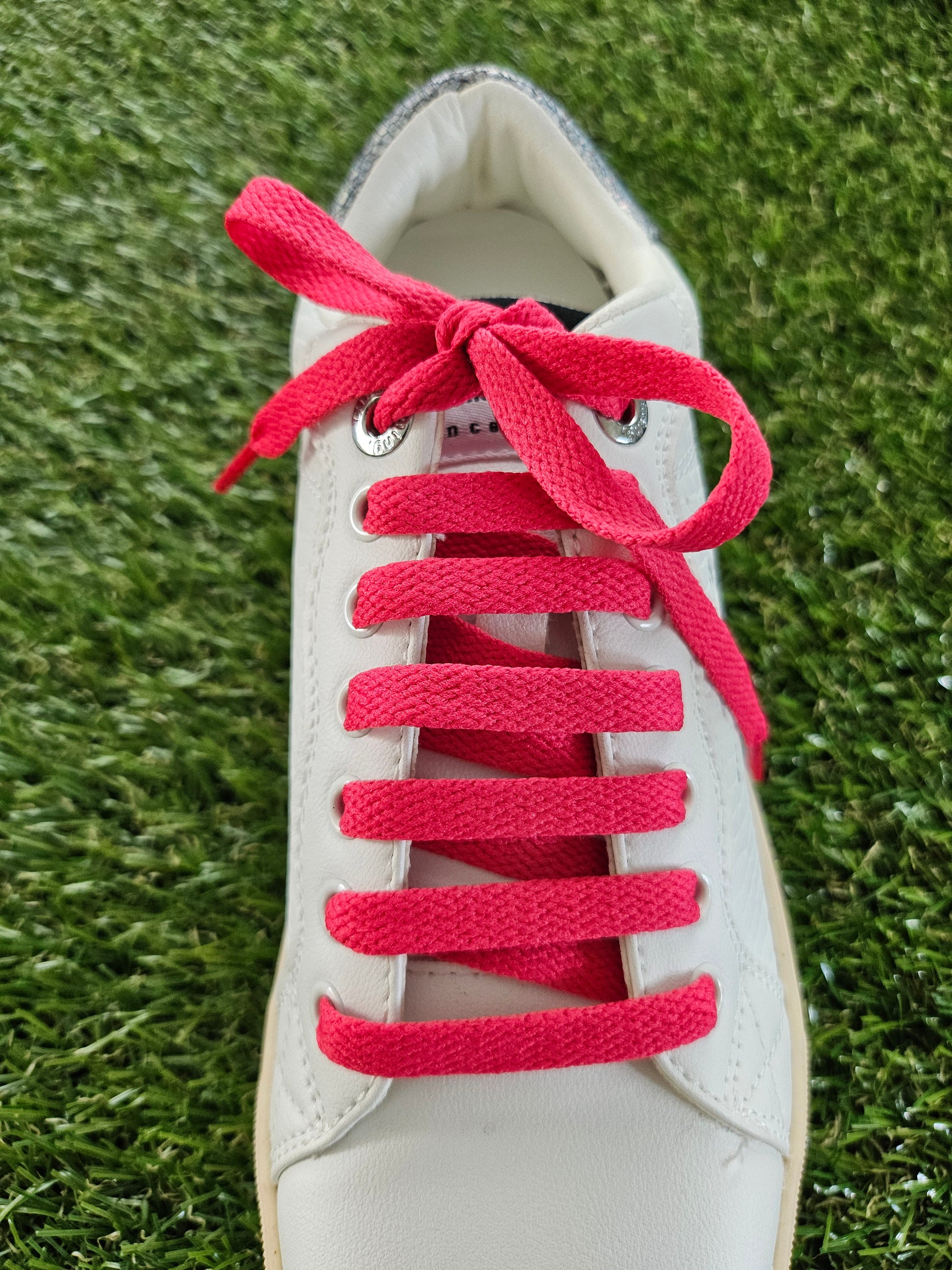 White trainer with watermelon red laces on a grass background