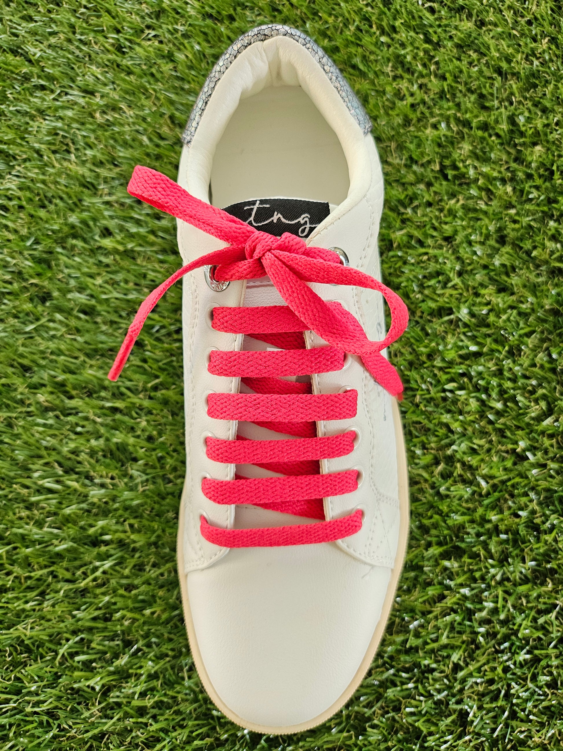 White trainer with watermelon red laces on a grass background
