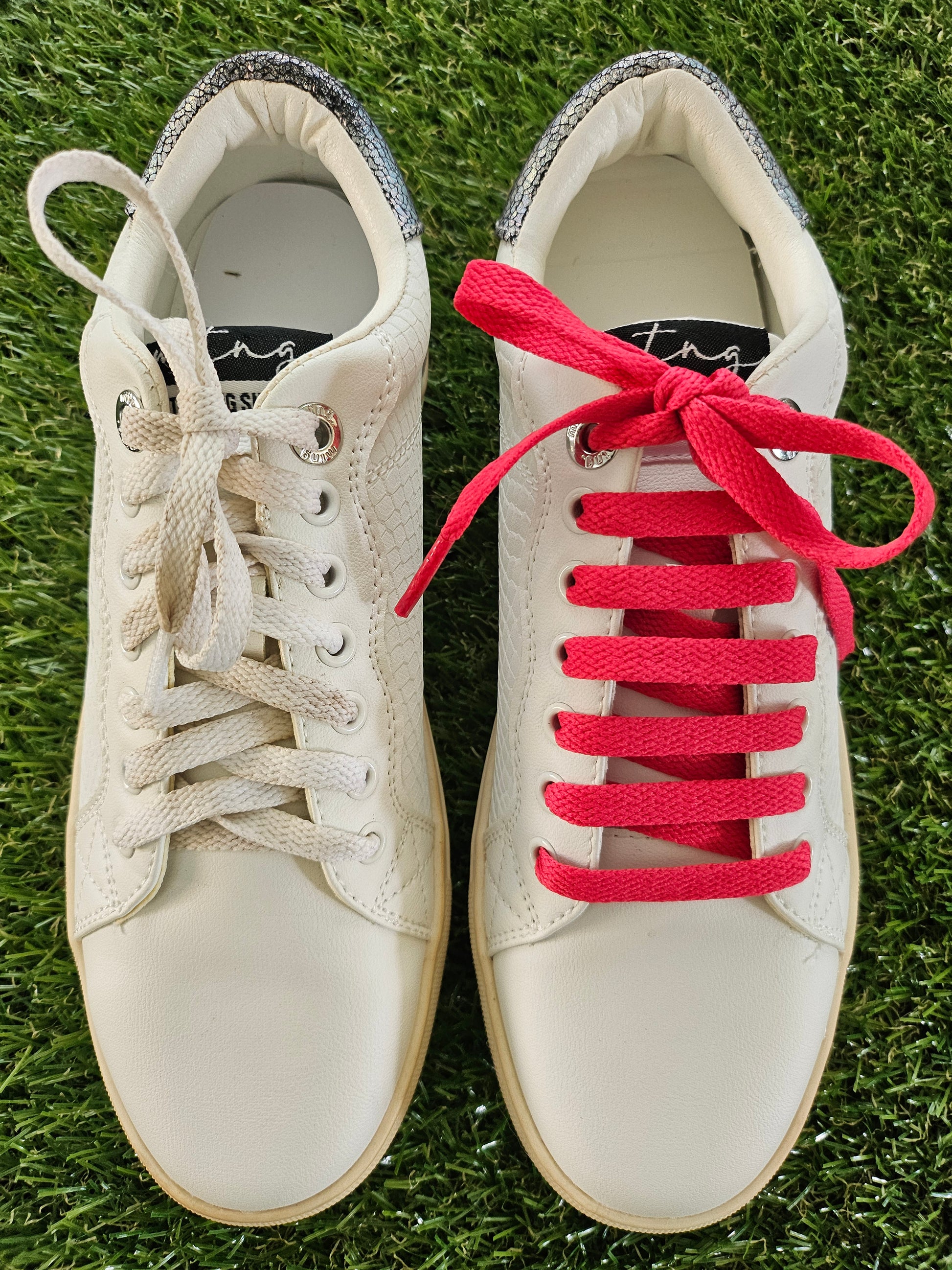 White trainer with watermelon red laces on a grass background