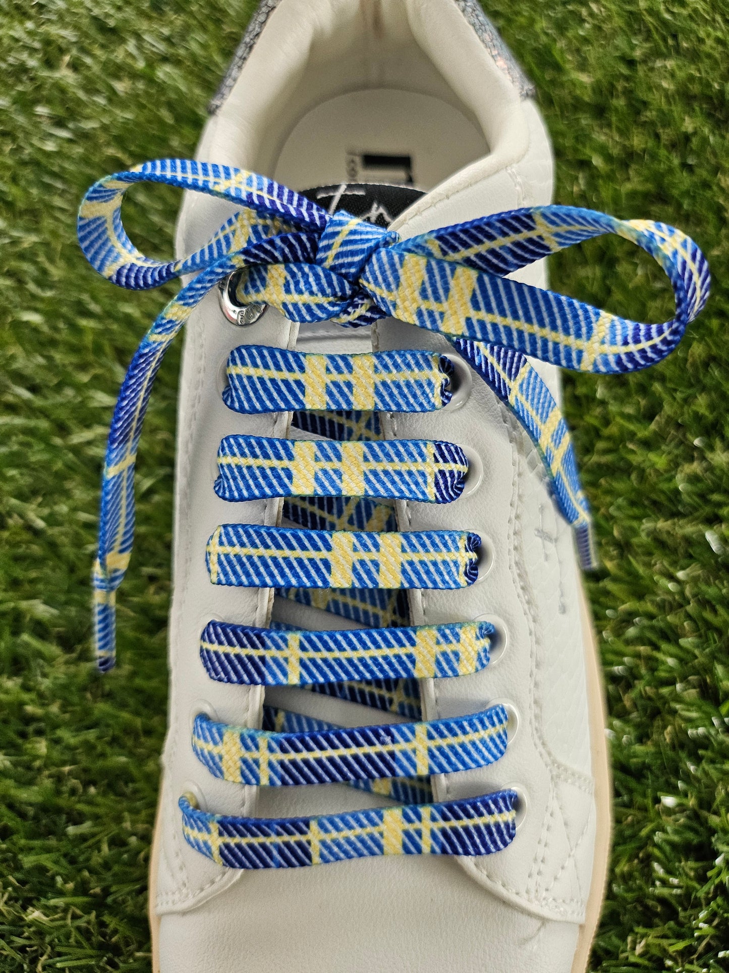 White sneaker with blue and yellow tartan laces on a grass background