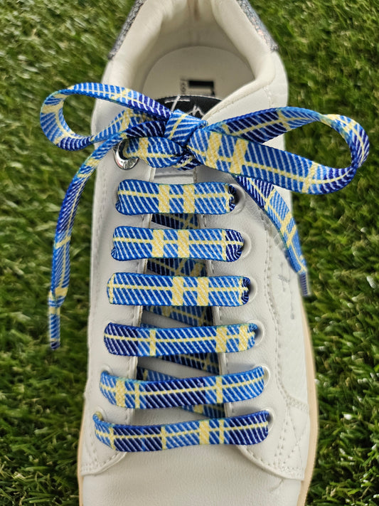 White sneaker with blue and yellow tartan laces on a grass background