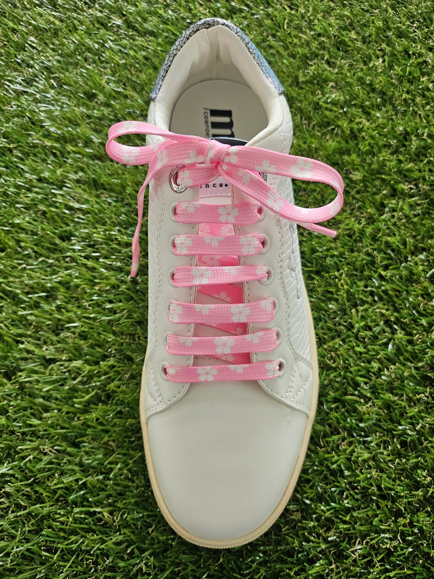 White sneaker with pink laces on a grass background