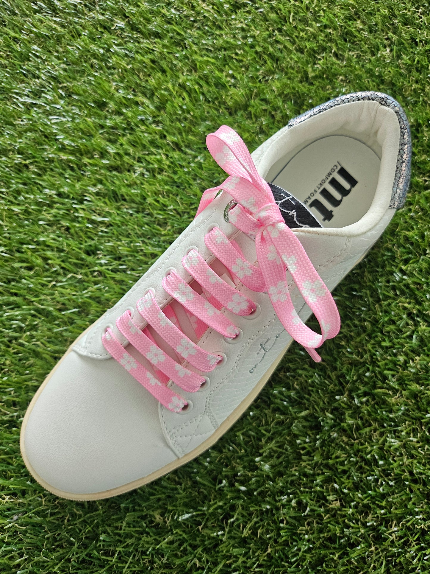 White trainer with pink shoelaces on grass
