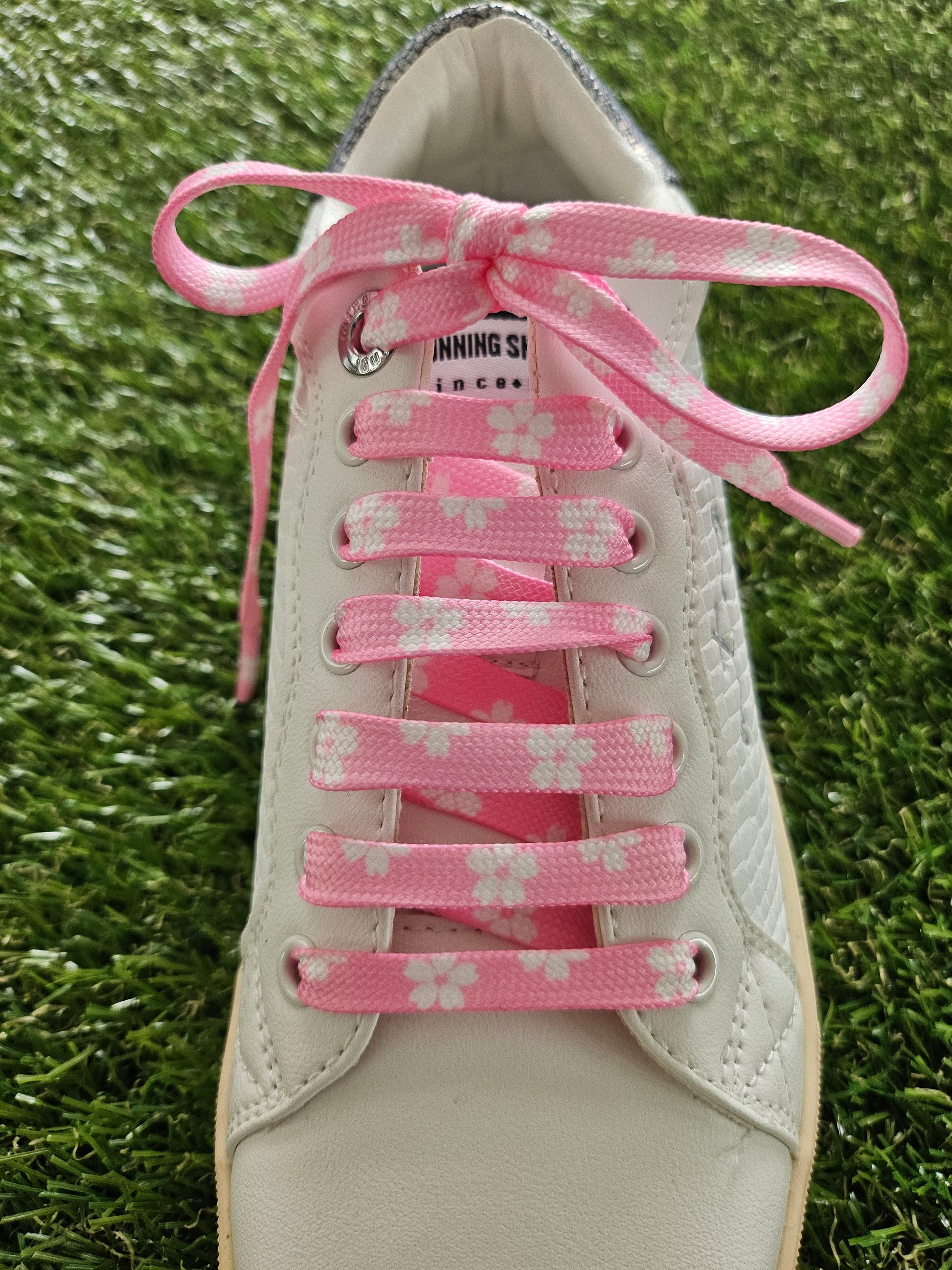 White sneaker with pink floral lace on a grass background