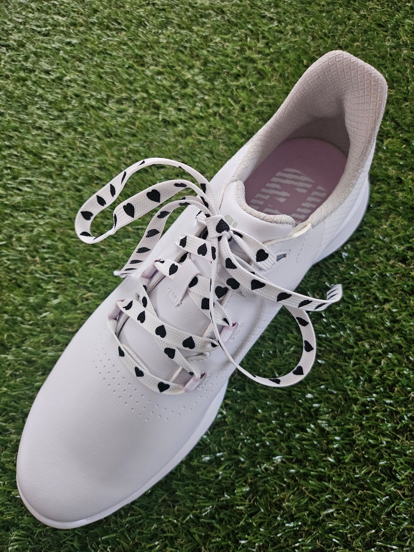 White golf shoe with white laces with black hearts on grass
