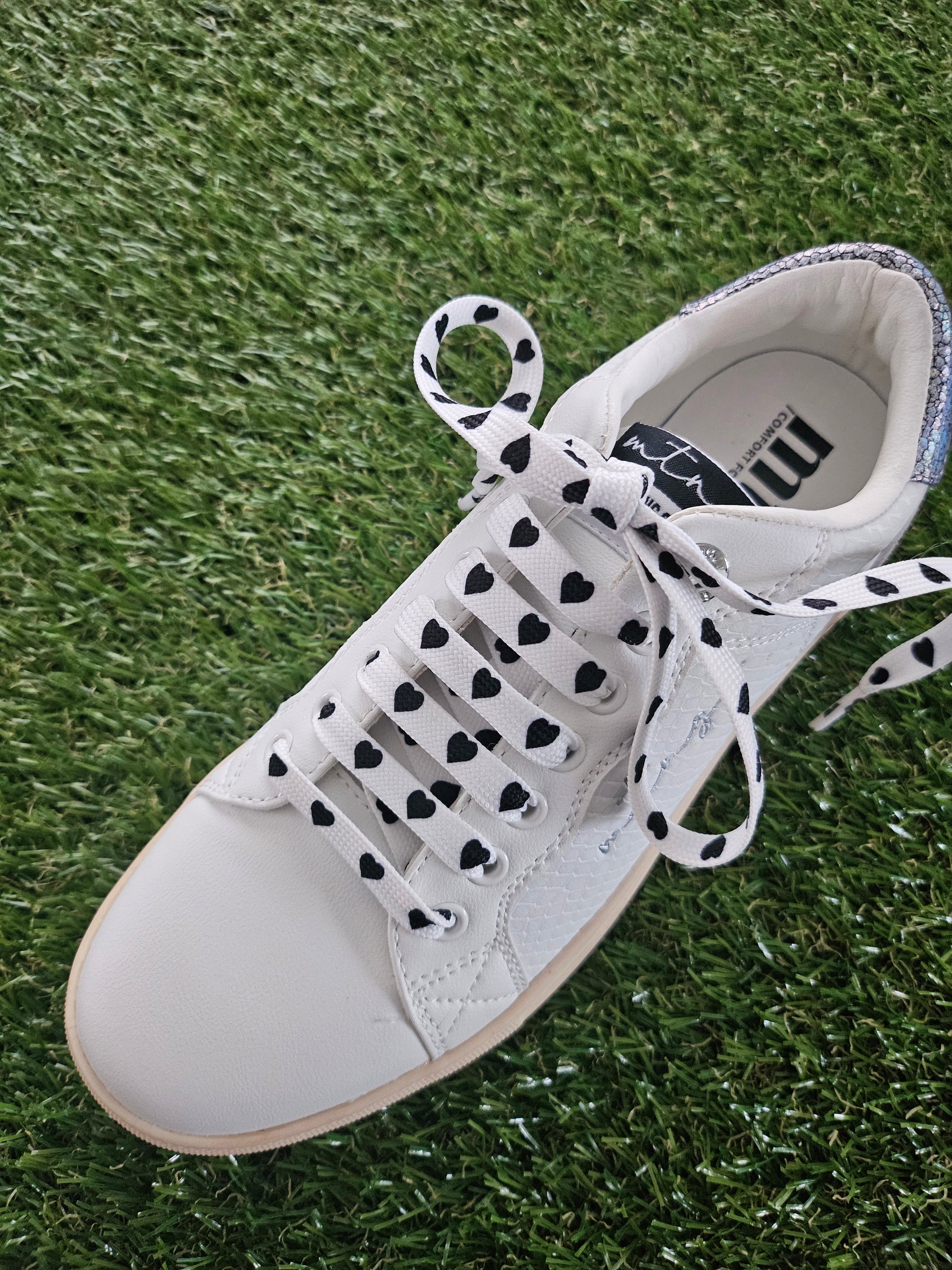 White sneaker with black heart patterns on laces on grass