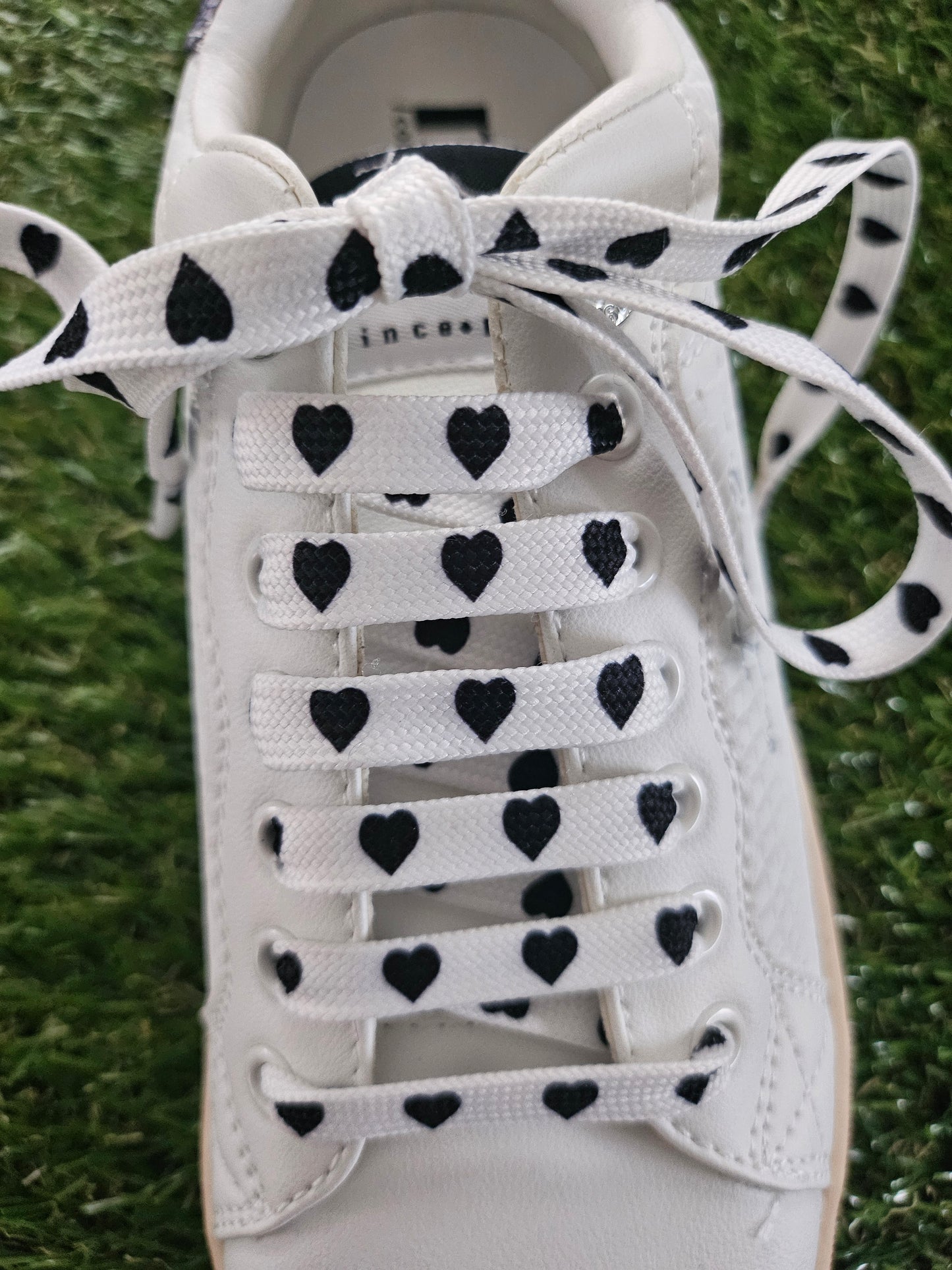 White trainer with black heart patterns on the laces against a grass background