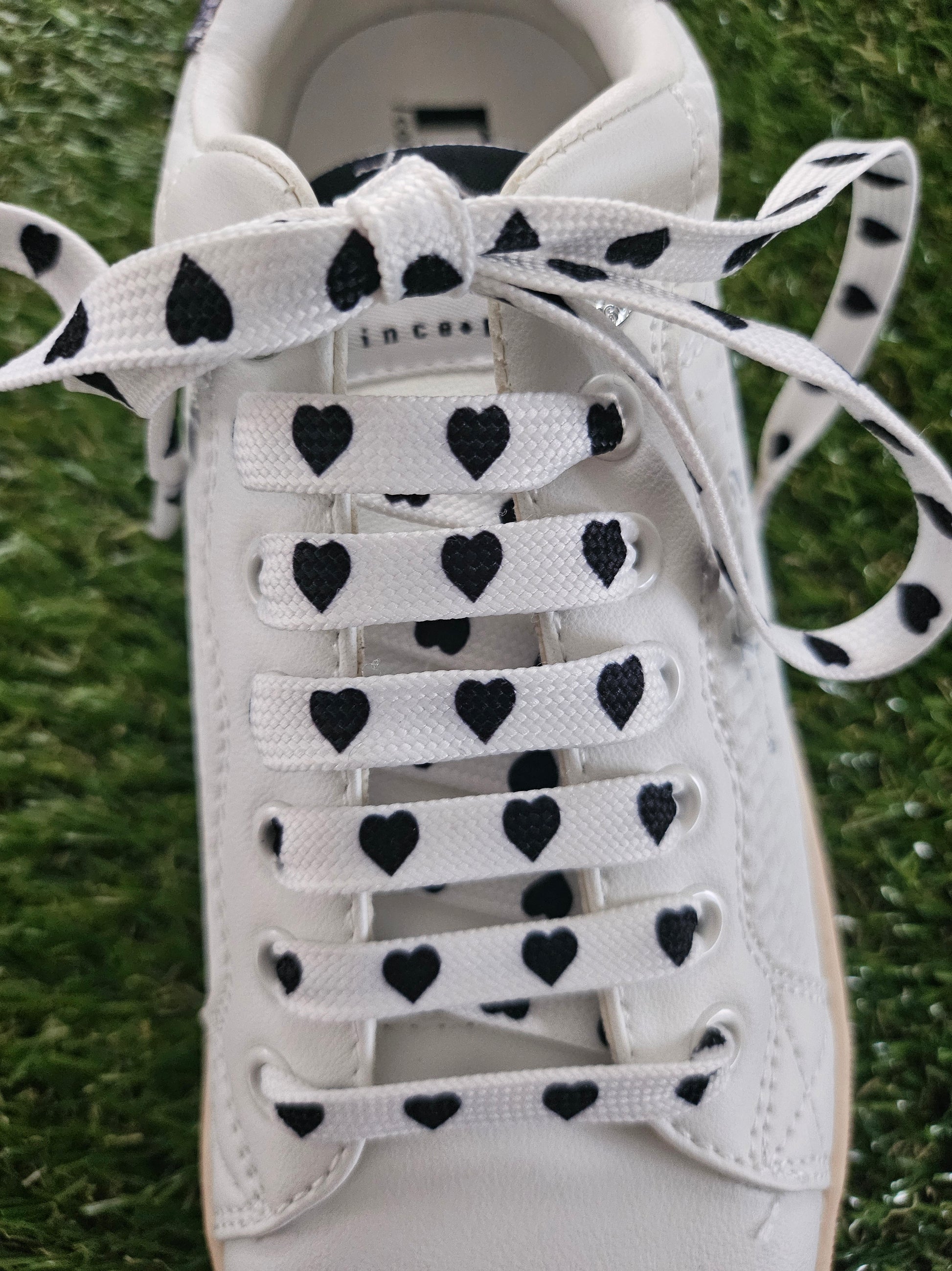 White trainer with black heart patterns on the laces against a grass background