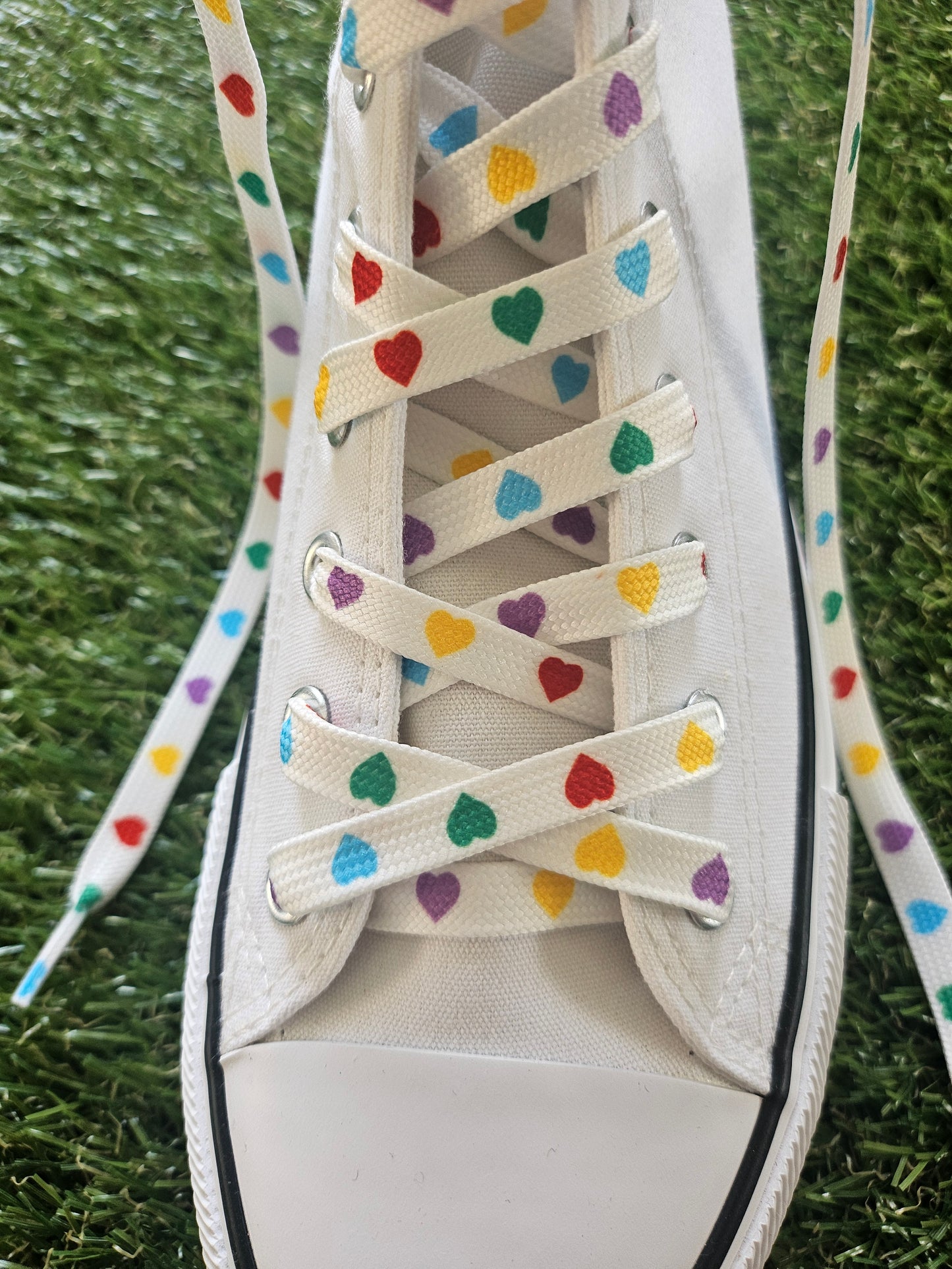 White sneaker with colorful heart-patterned laces on a grass background
