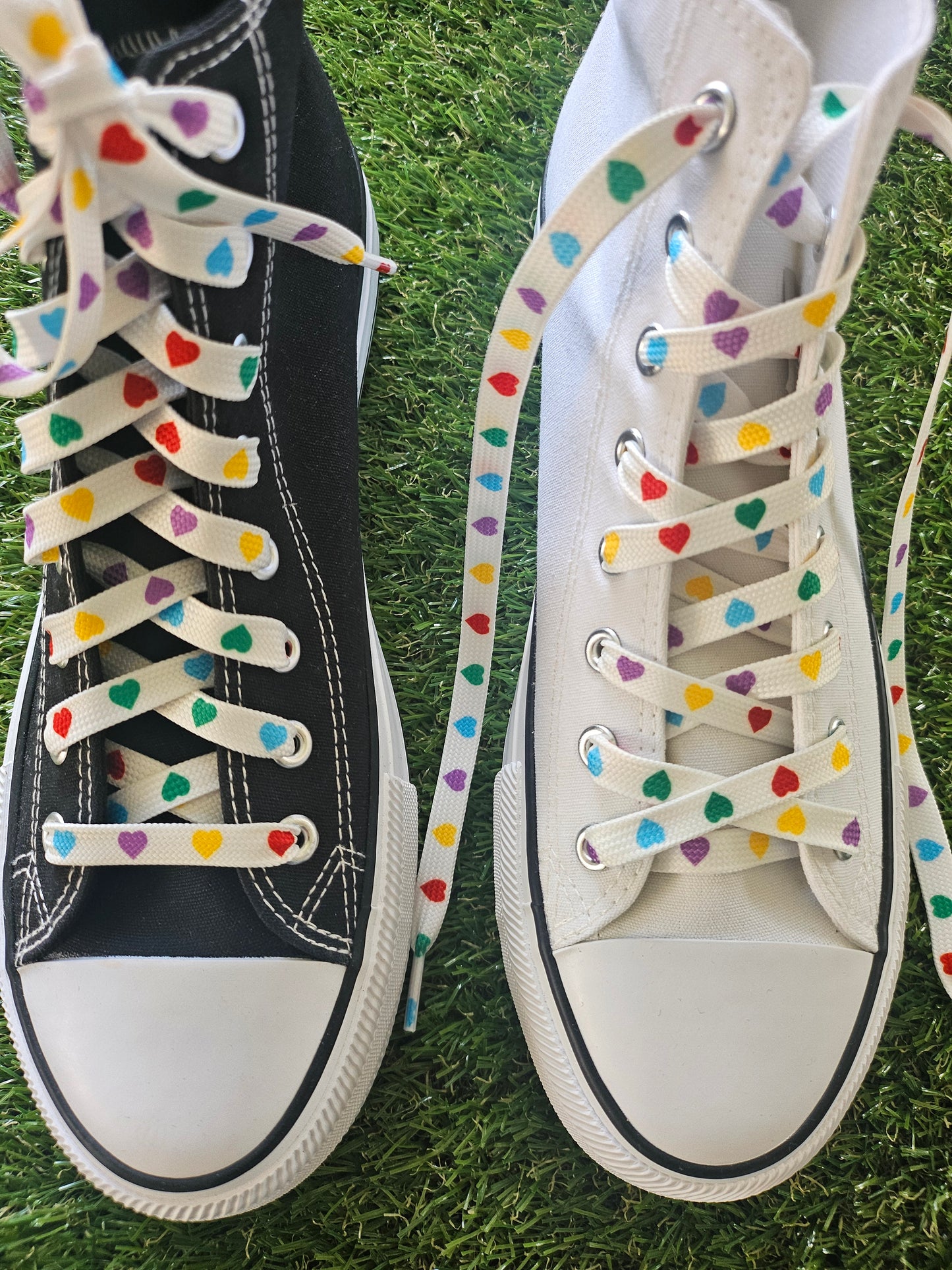 Pair of sneakers with colourful polka hearts shoelaces on a grass background