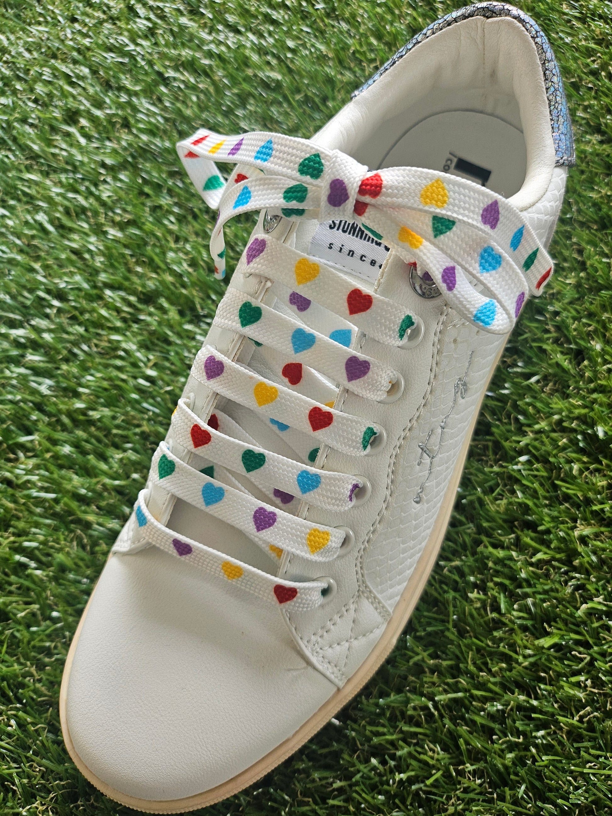 White sneaker with colorful heart-patterned laces on a grass background