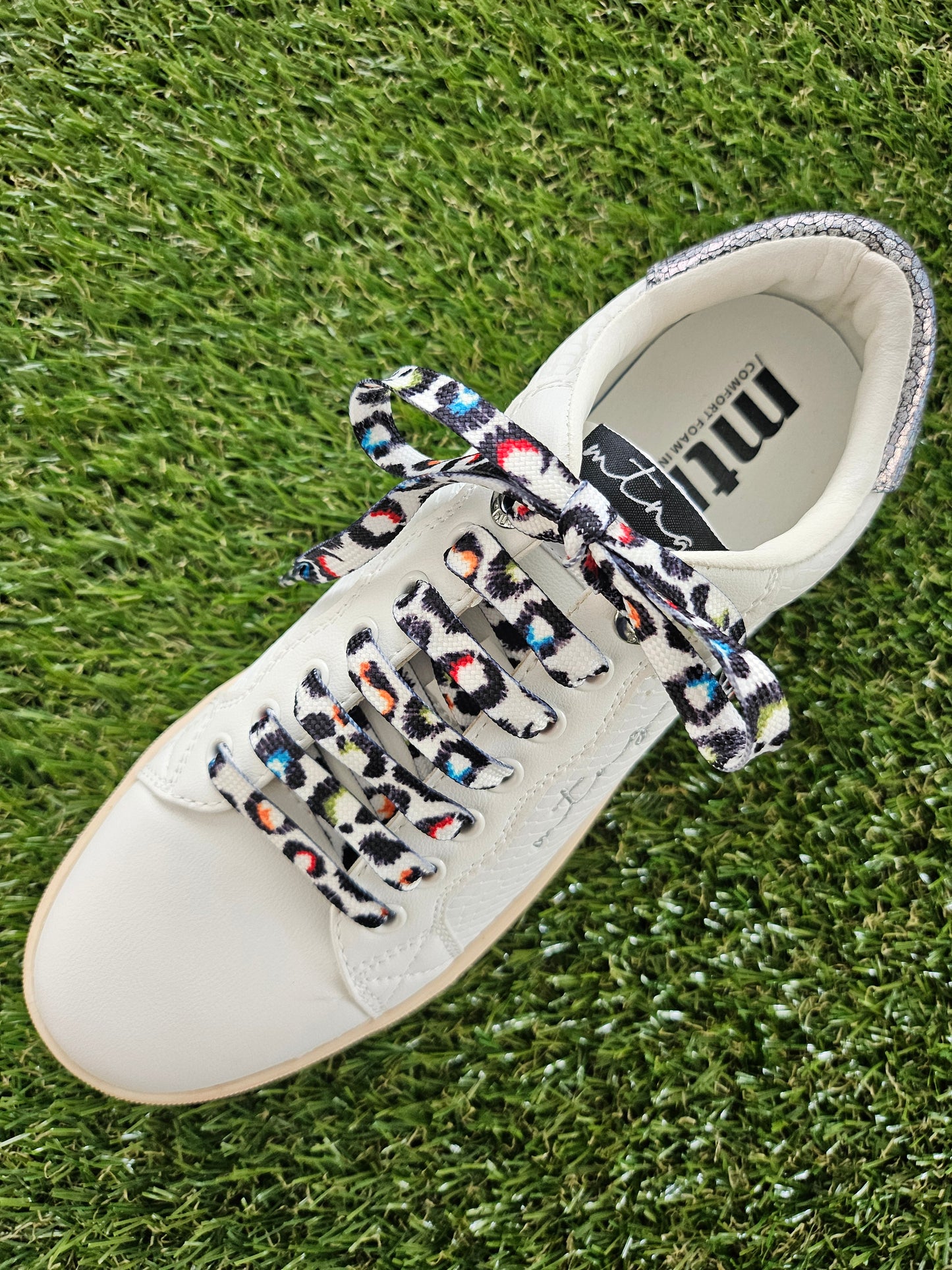 White sneaker with colorful leopard print laces on grass