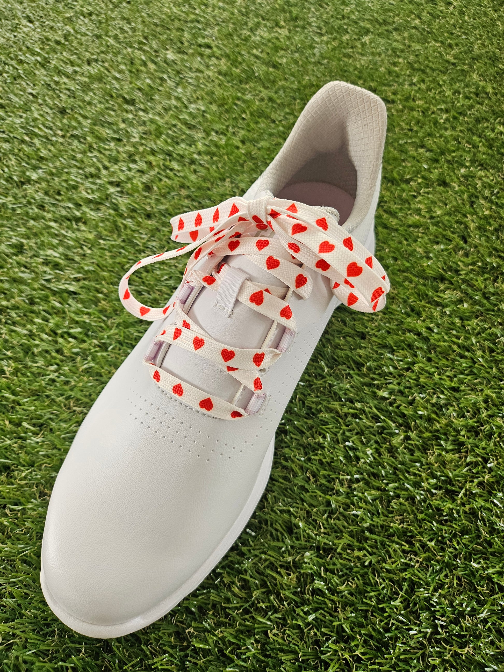 White ladies golf shoe with red heart-patterned laces on a grass background