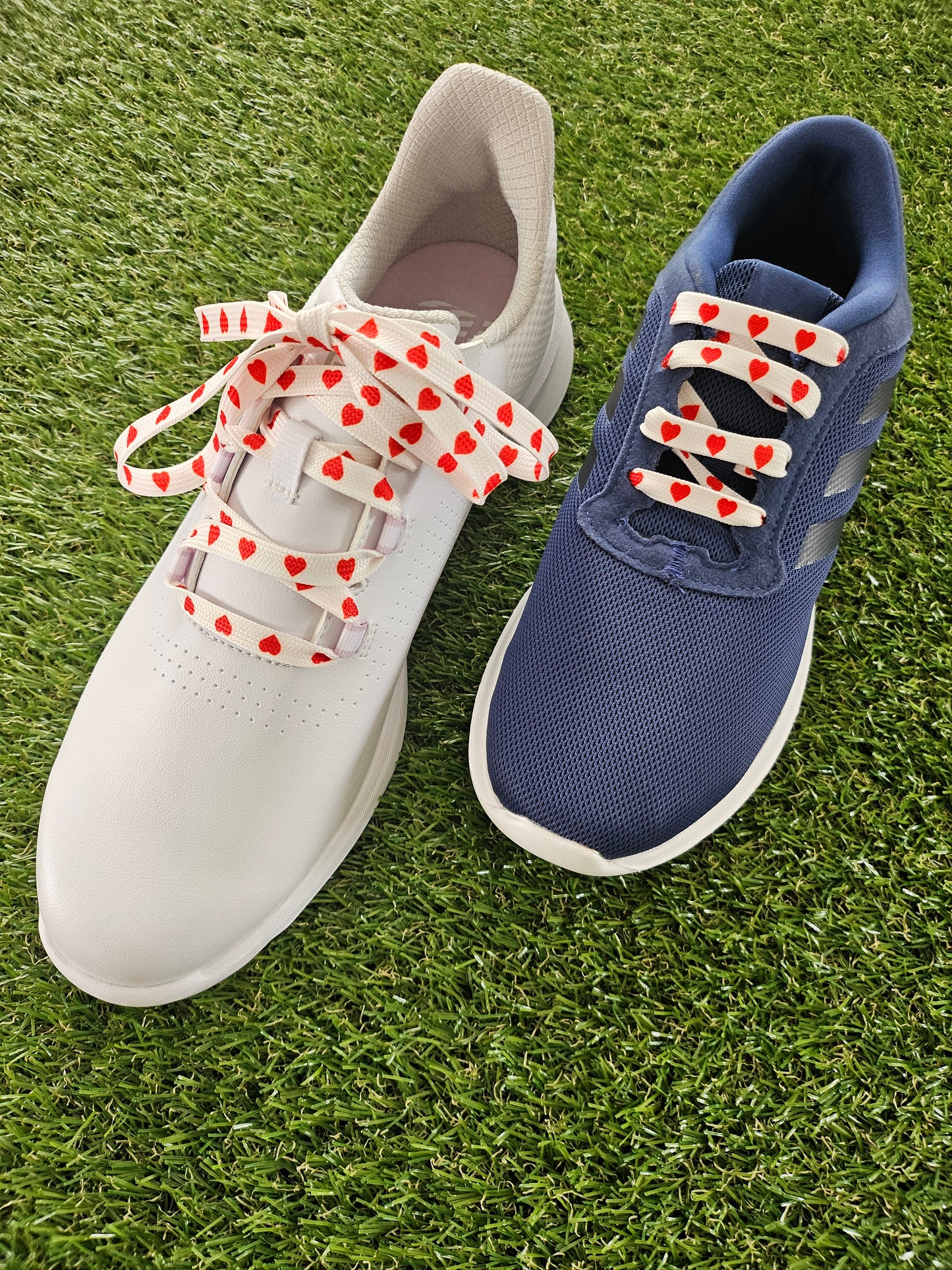 Two trainers with red love heart laces on a grass background