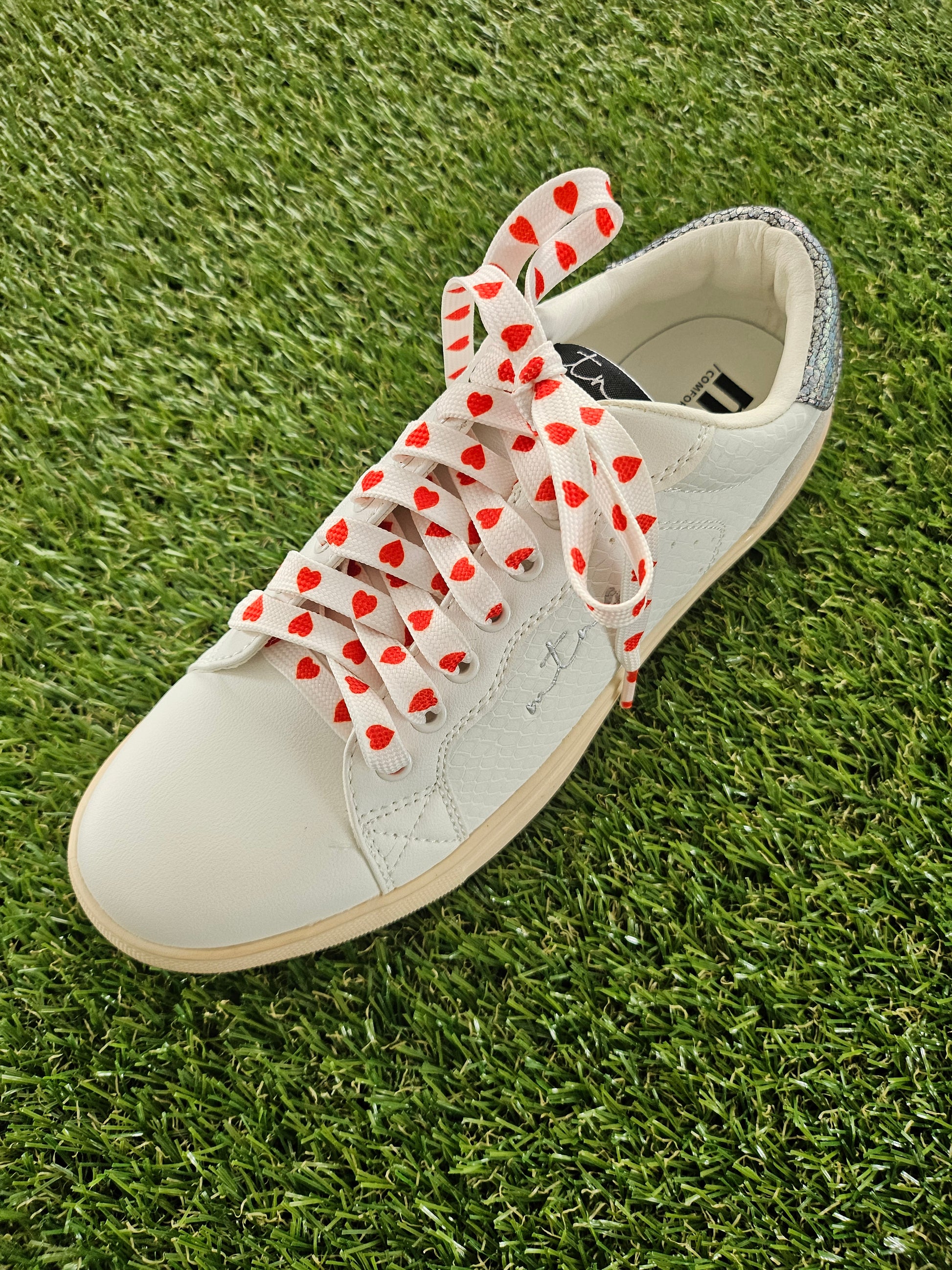 White trainer with red heart-patterned laces on grass