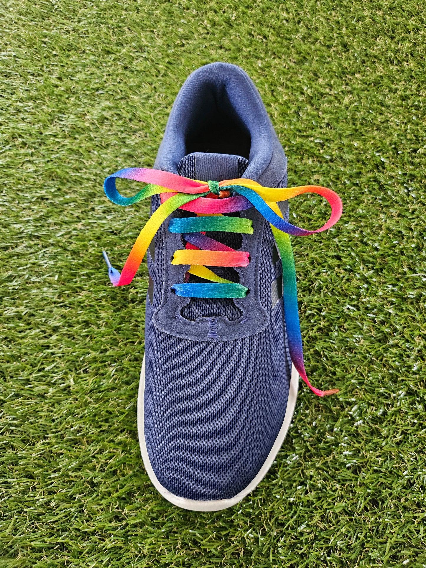 Navy blue sneaker with colourful rainbow shoelaces on grass