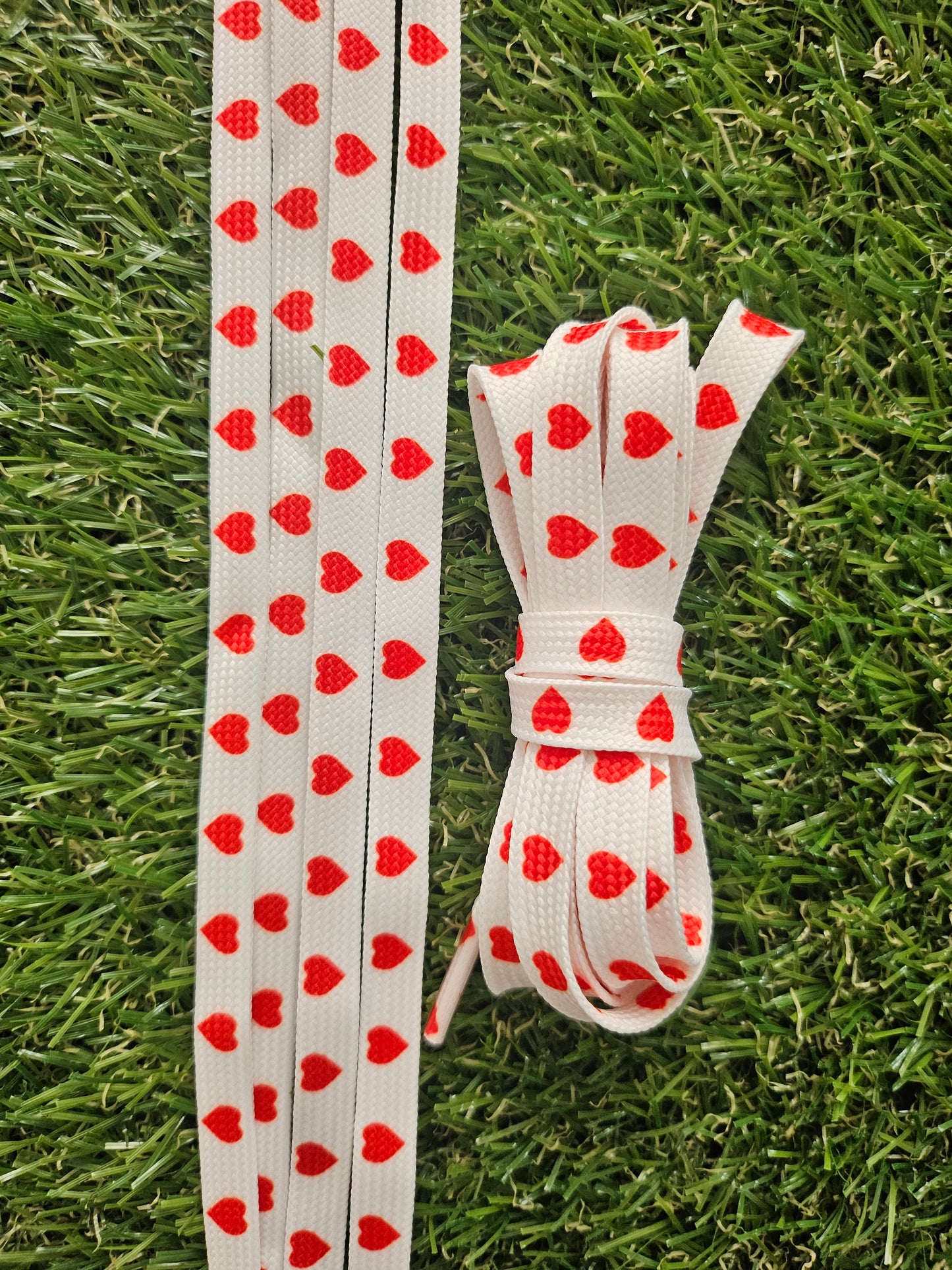 White shoelaces with red lovehearts on a grass background