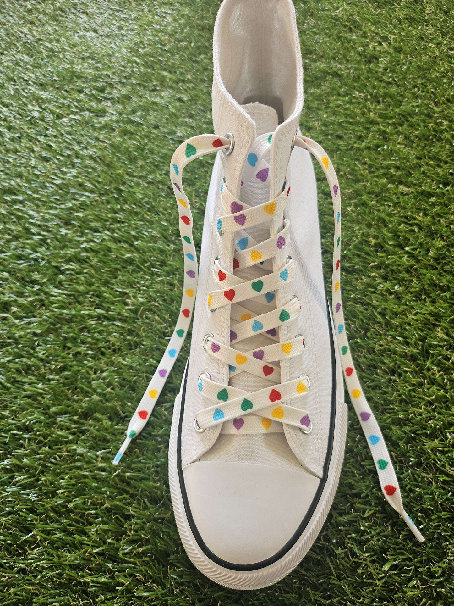 White sneaker with colourful love heart laces on a grass background