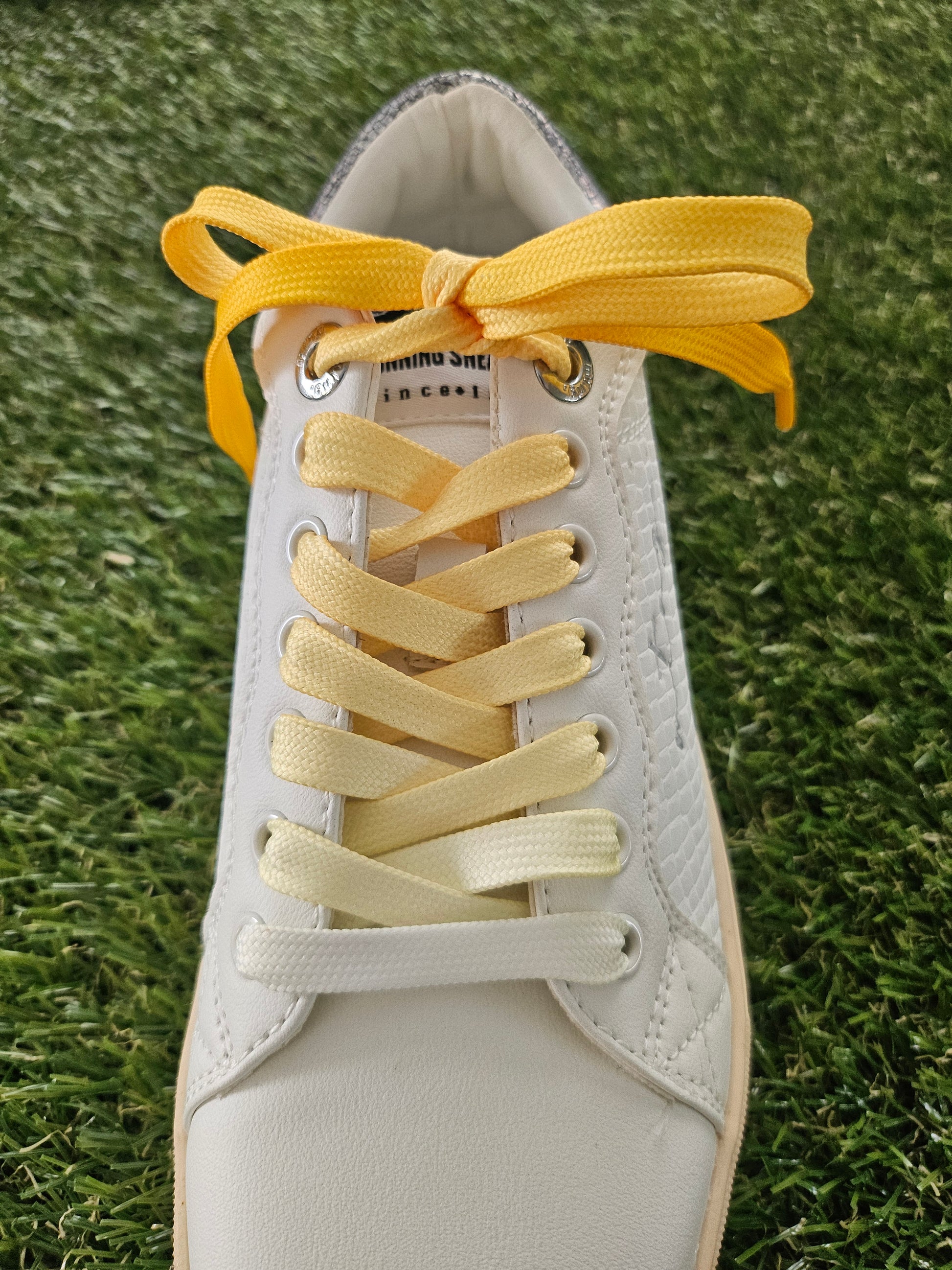 White sneaker with yellow shoelaces on a grass background