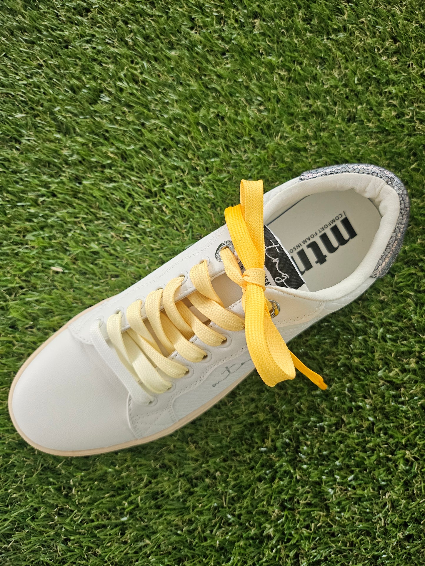White sneaker with yellow shoelaces on grass