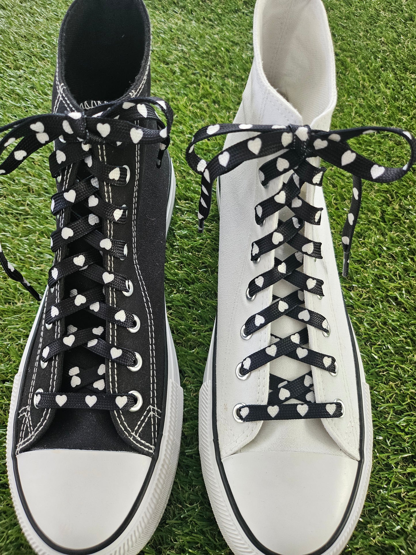 a black and a white converse high top boot on grass with black shoelaces with a white heart pattern