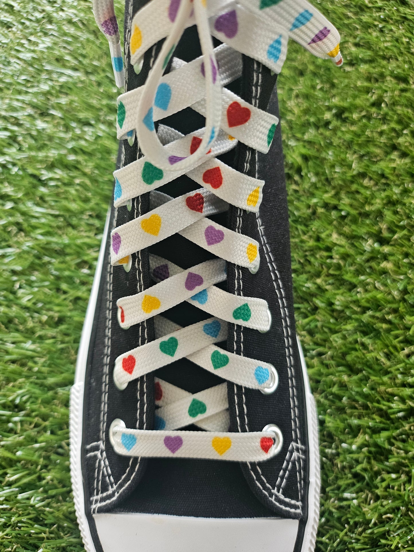 Black trainer with colorful heart-patterned laces on grass