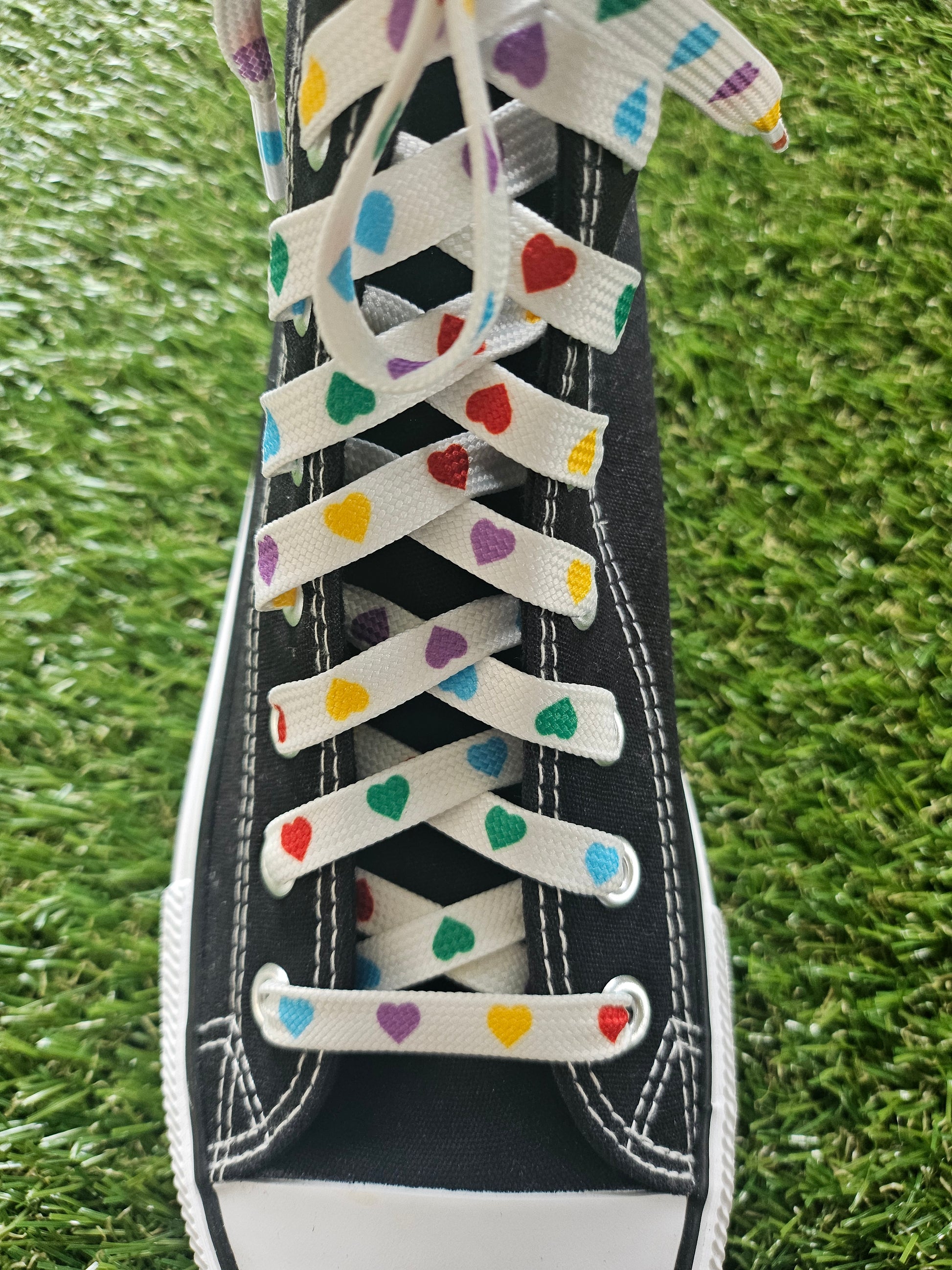 Black trainer with colorful heart-patterned laces on grass