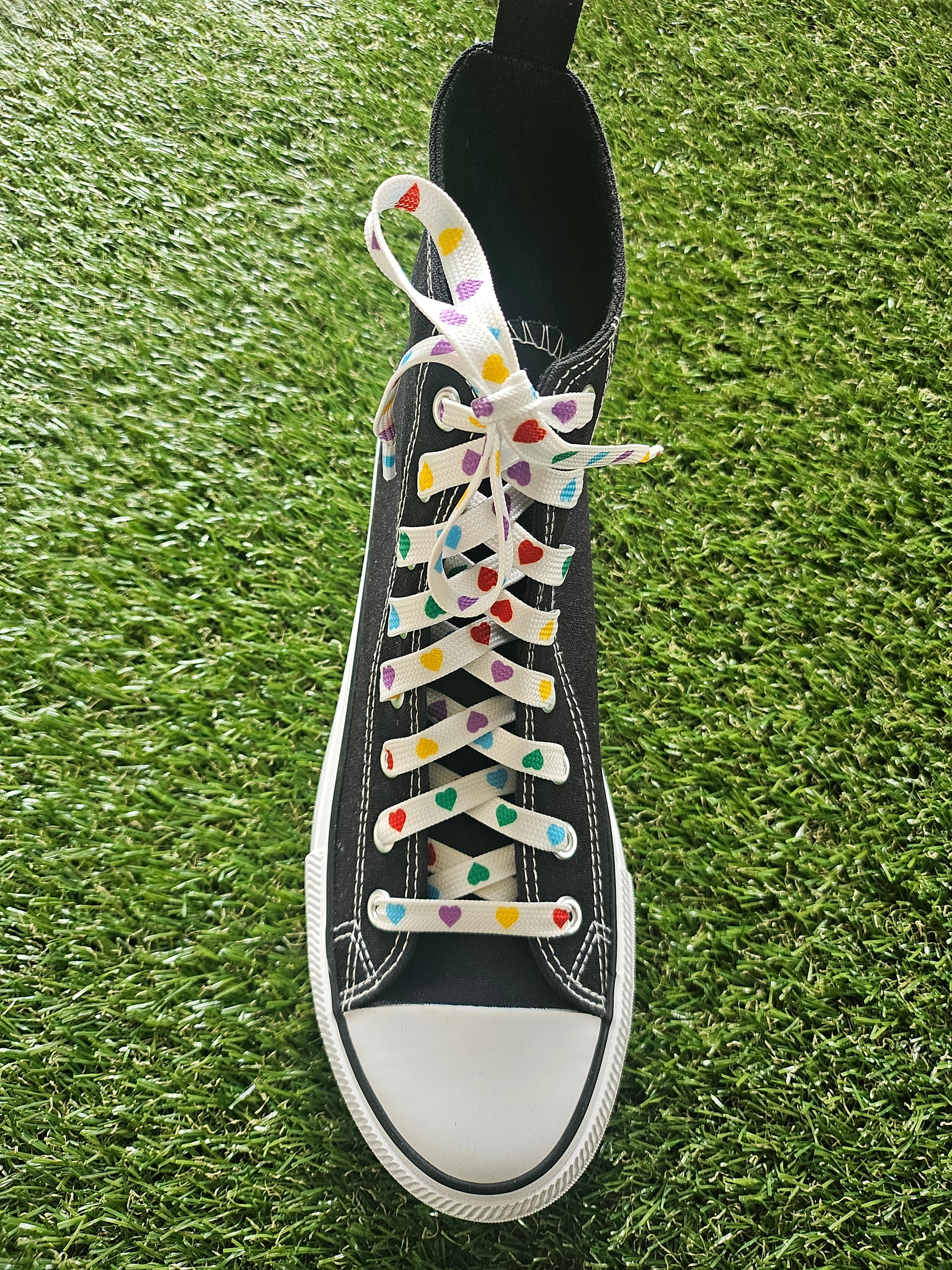 Black trainer with colorful heart-patterned laces on grass