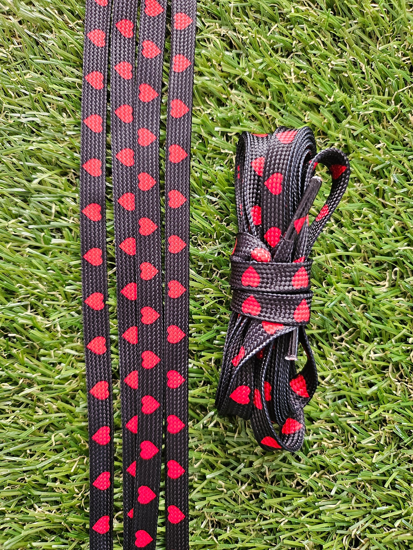 Black shoe laces with red heart pattern on grass
