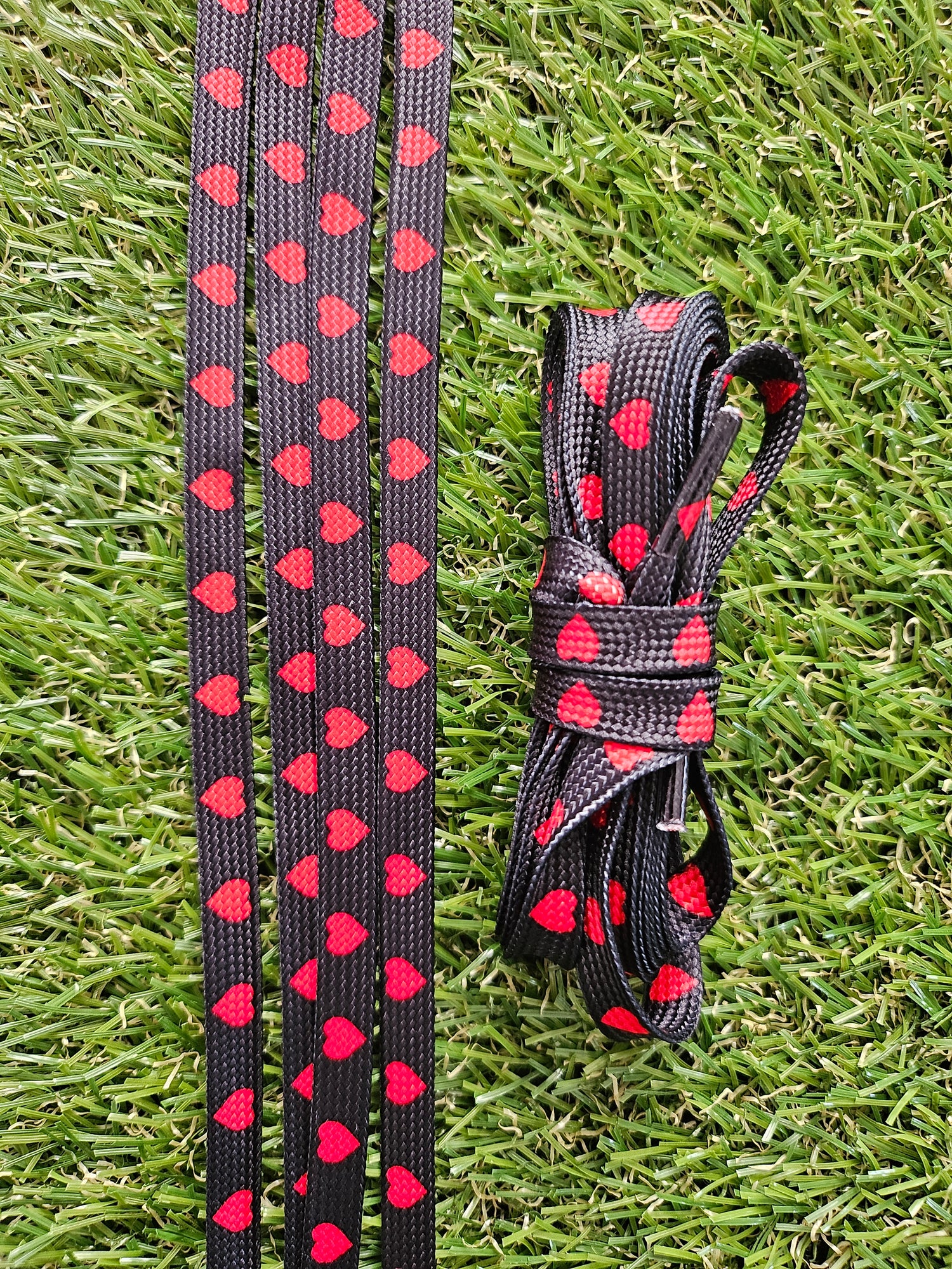 Black shoe laces with red heart pattern on grass