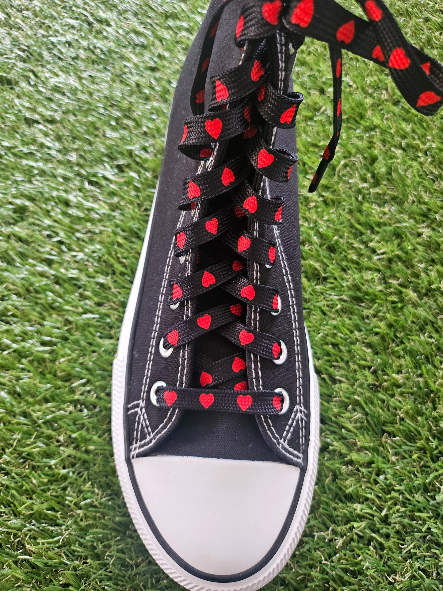 Black sneaker with red heart-shaped laces on grass