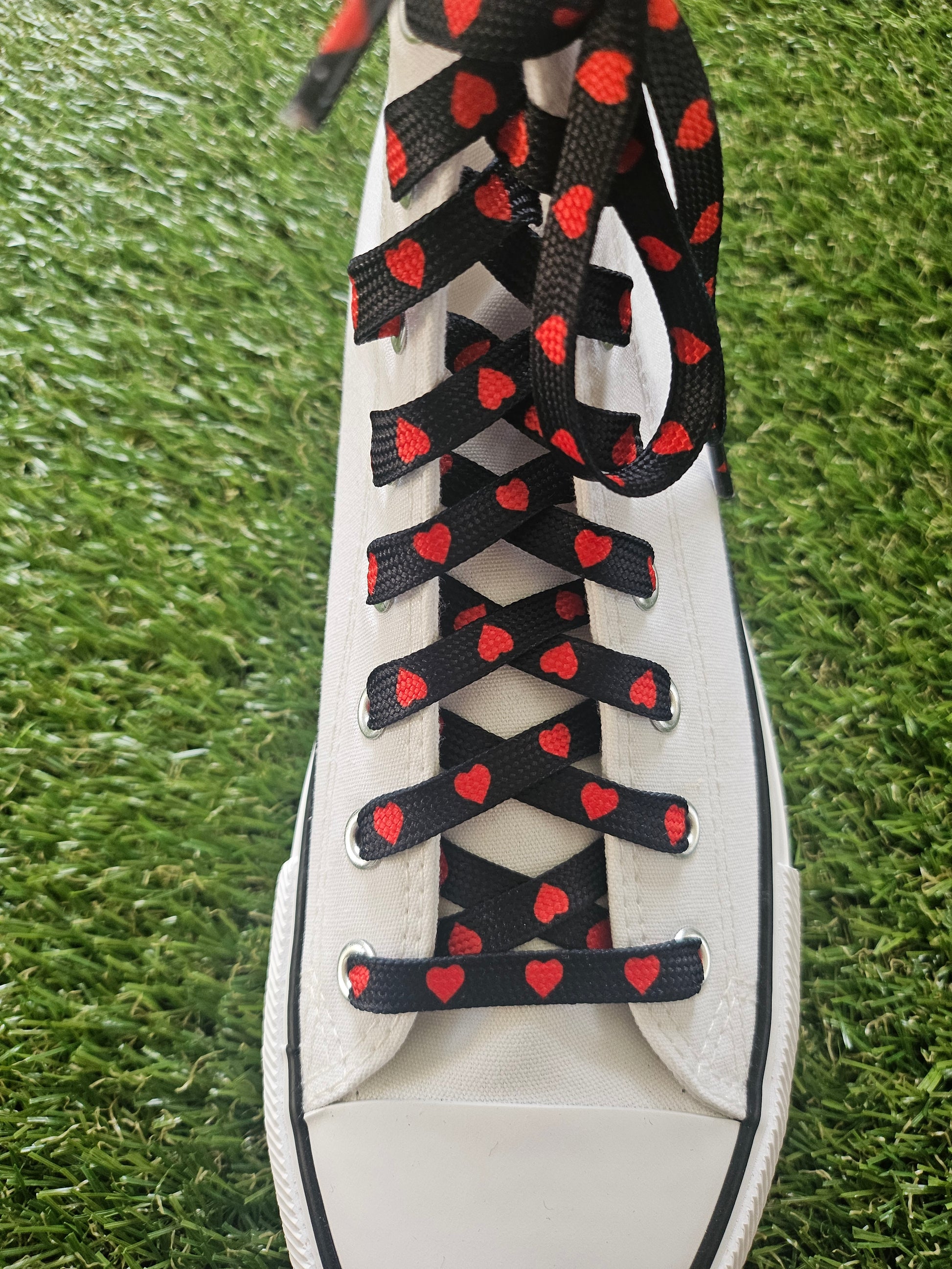 White sneaker with black and red heart-patterned laces on a grass background