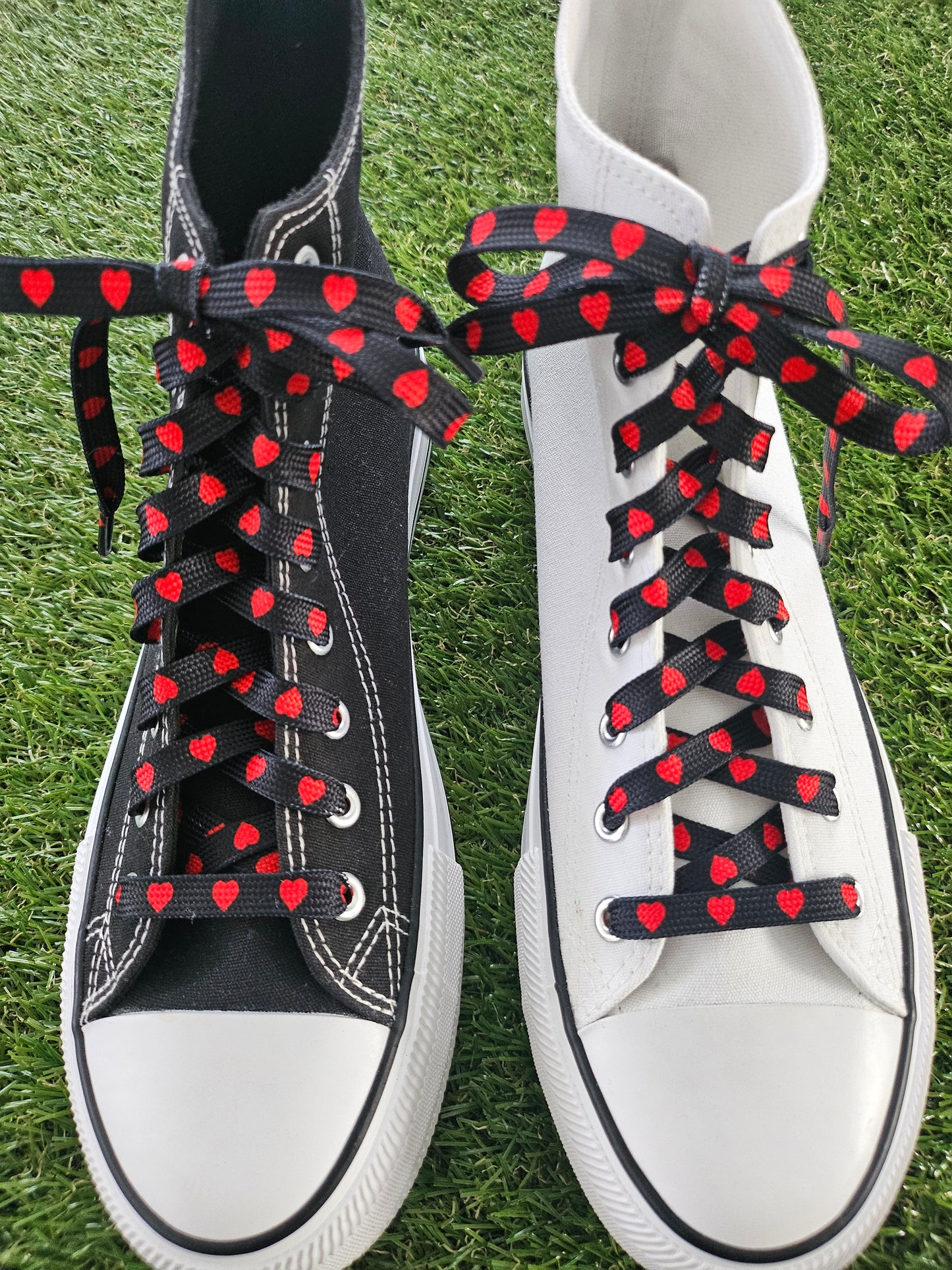 White sneakers with black and red heart-patterned laces on a grass background