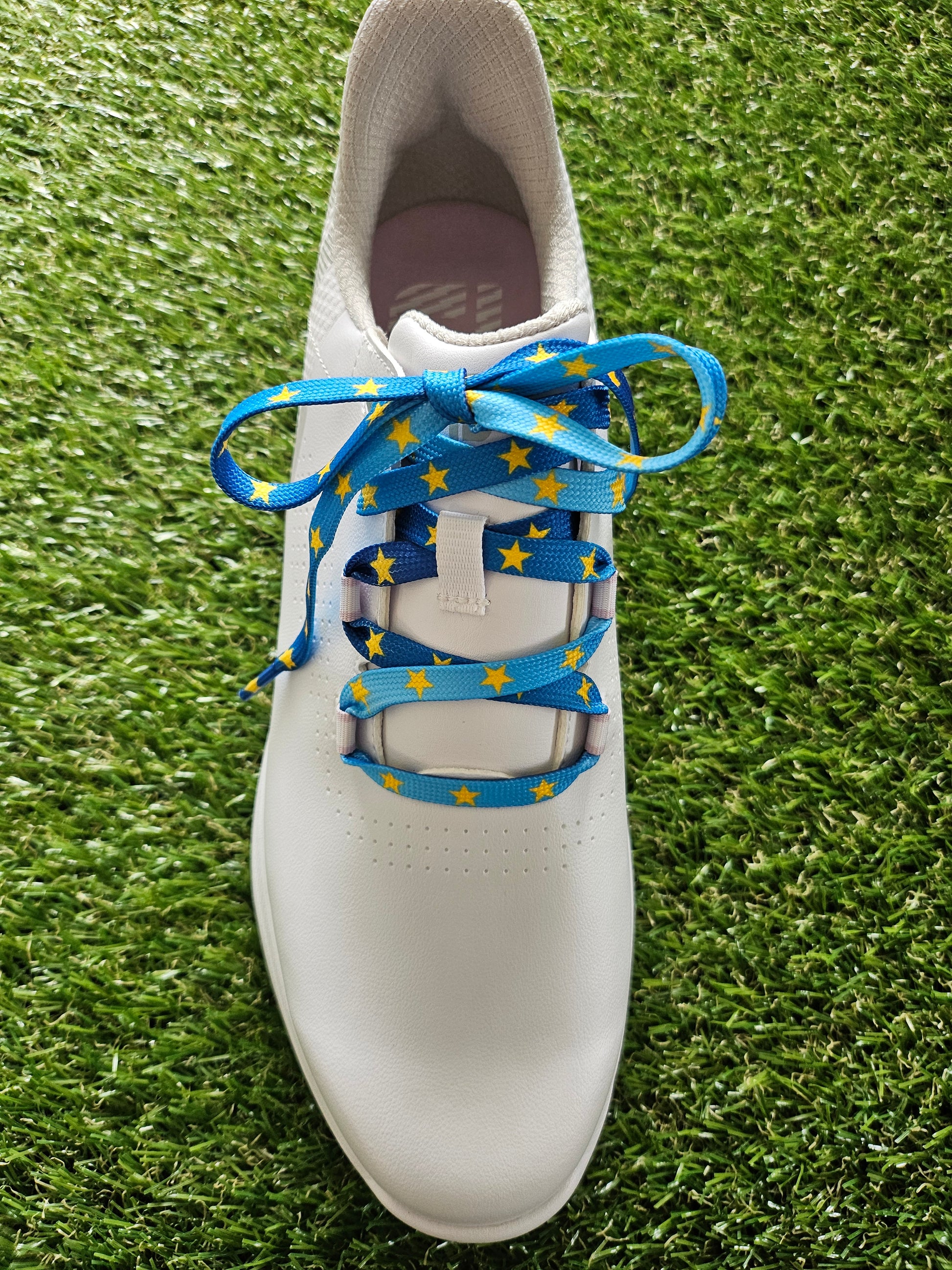 White golf shoe with blue shoelaces featuring yellow stars on a grass background