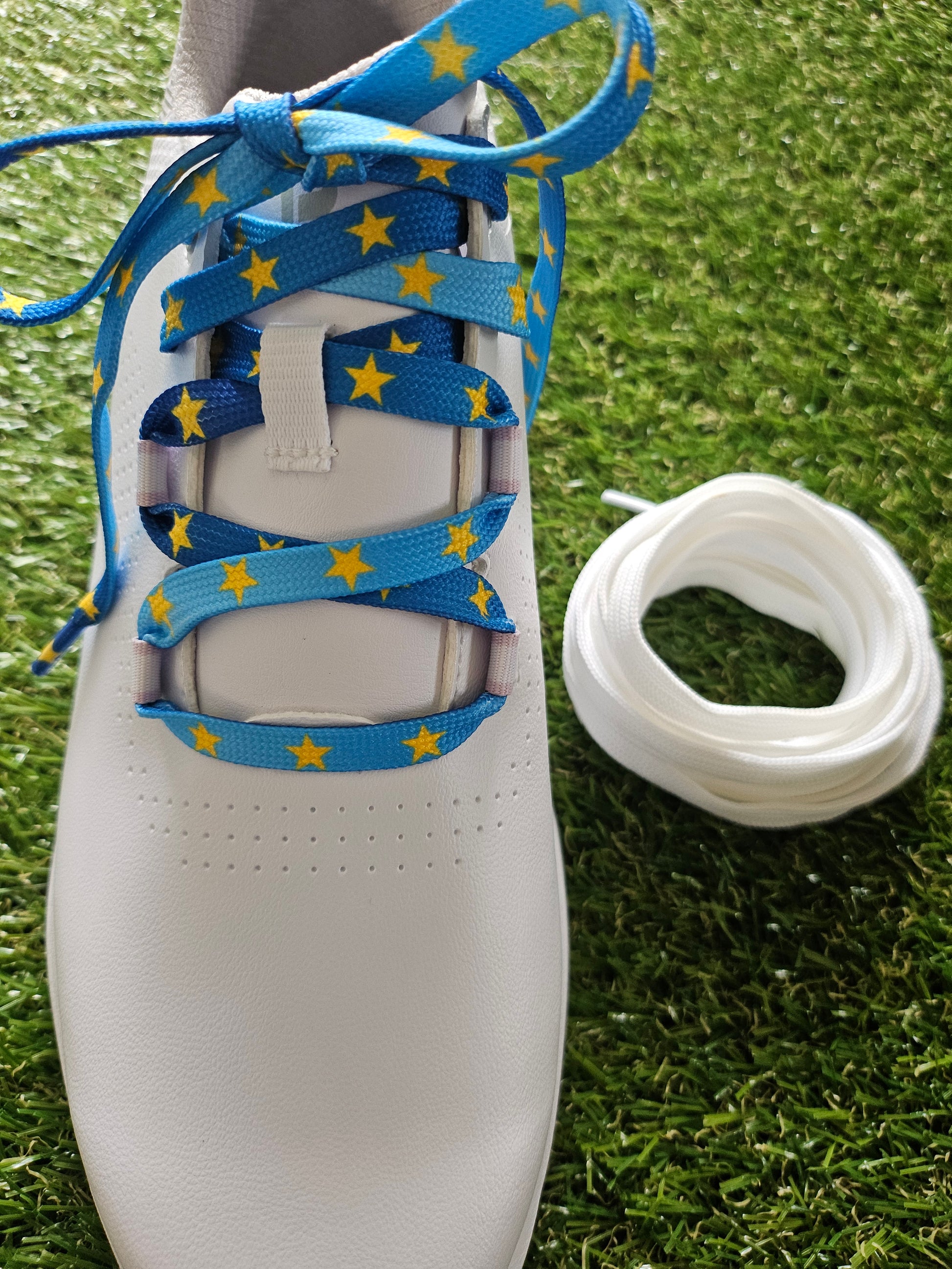 White golf shoe with blue shoelaces featuring yellow stars on grass