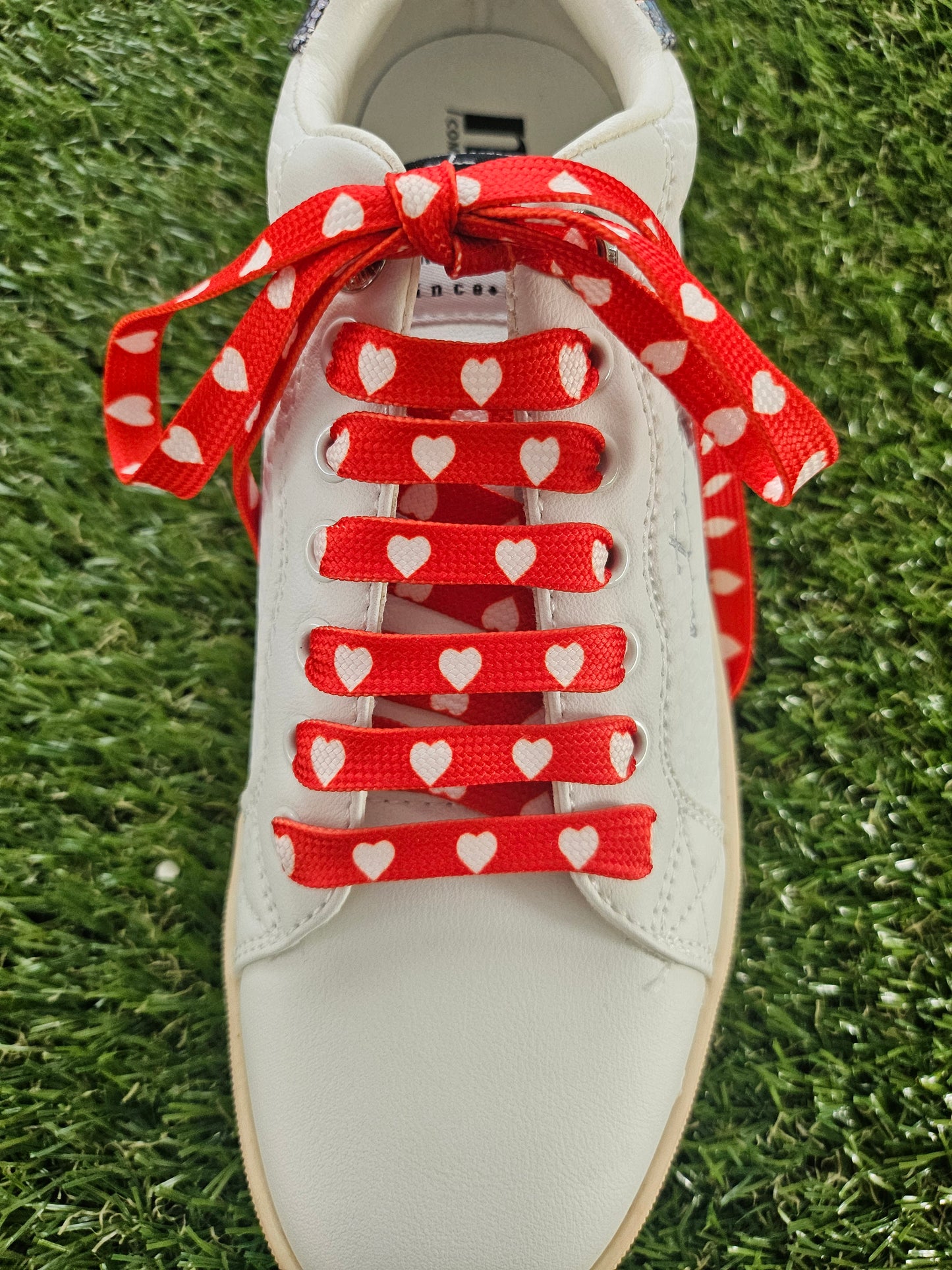 White sneaker with red shoelaces featuring heart patterns on a grass background