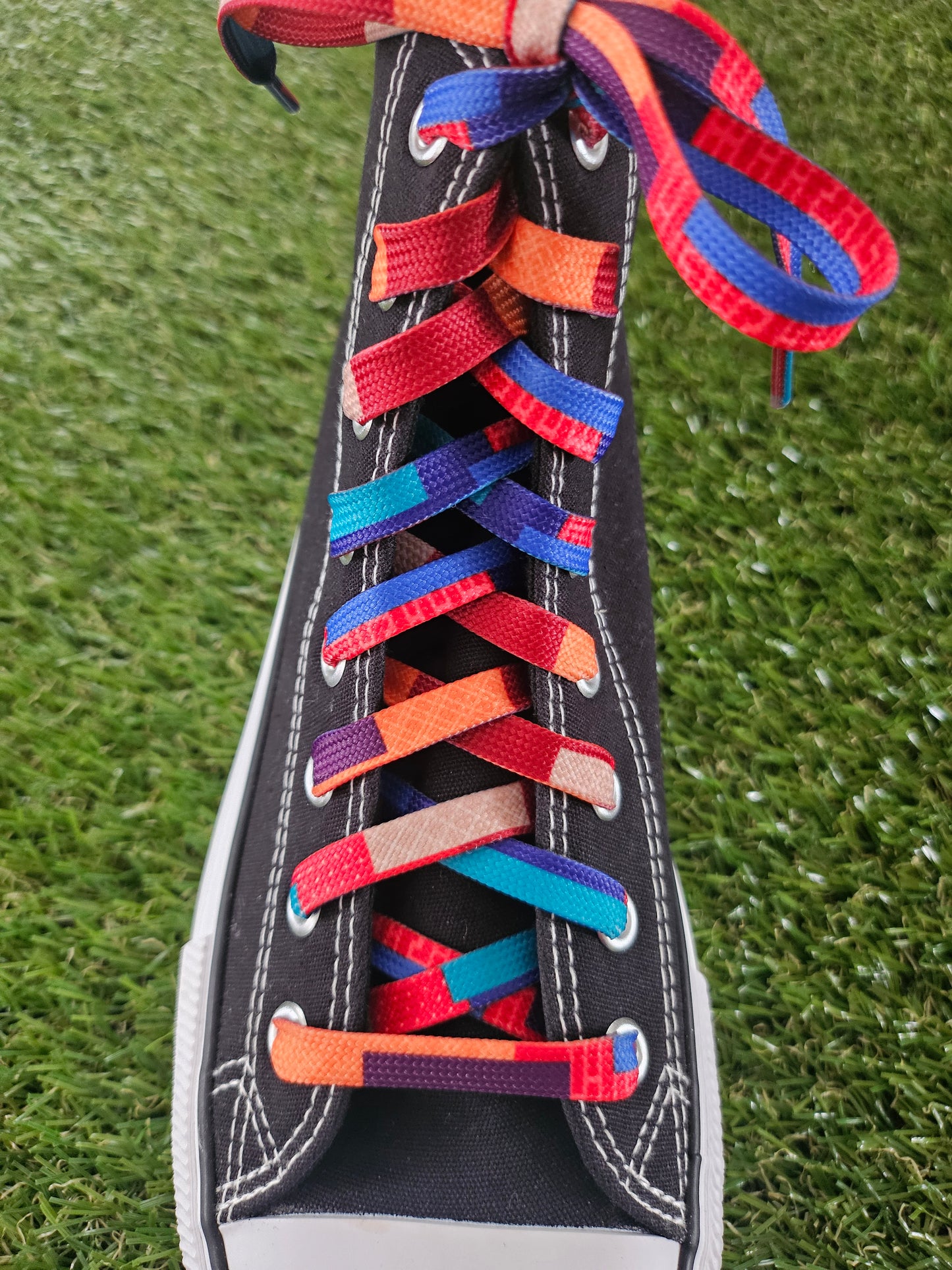 Colorful shoelaces on a black sneaker against a grass background