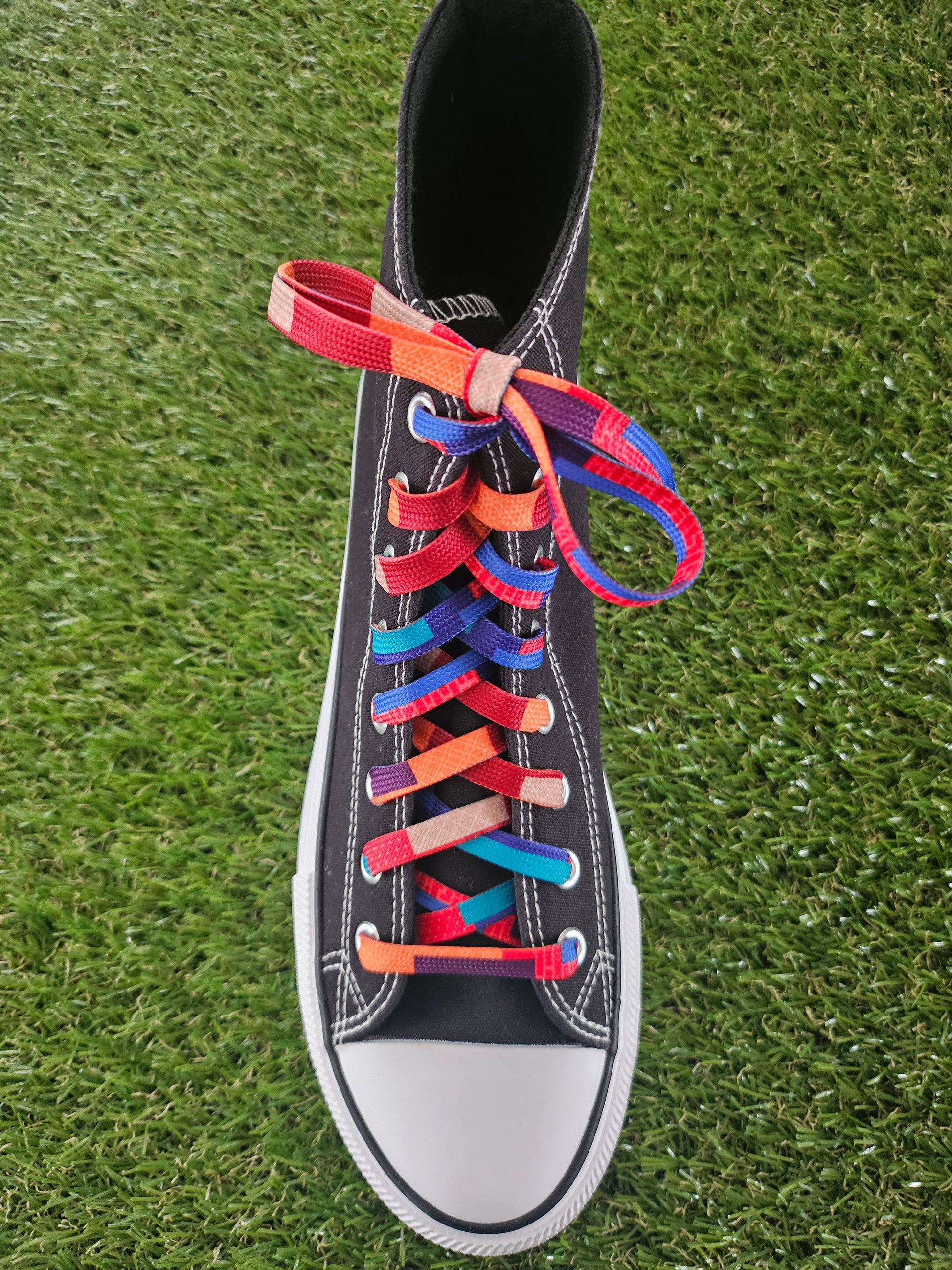 Black high-top sneaker with colourful laces on a grass background