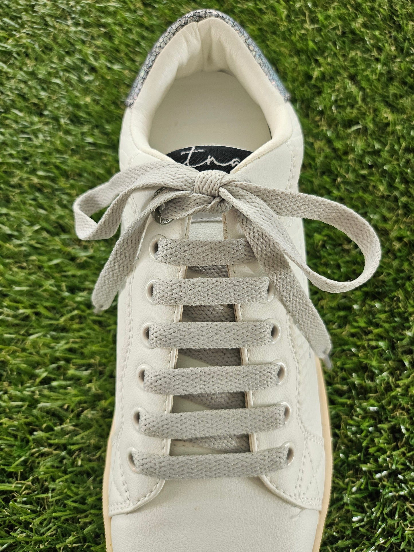 White sneaker with gray laces on a grass background
