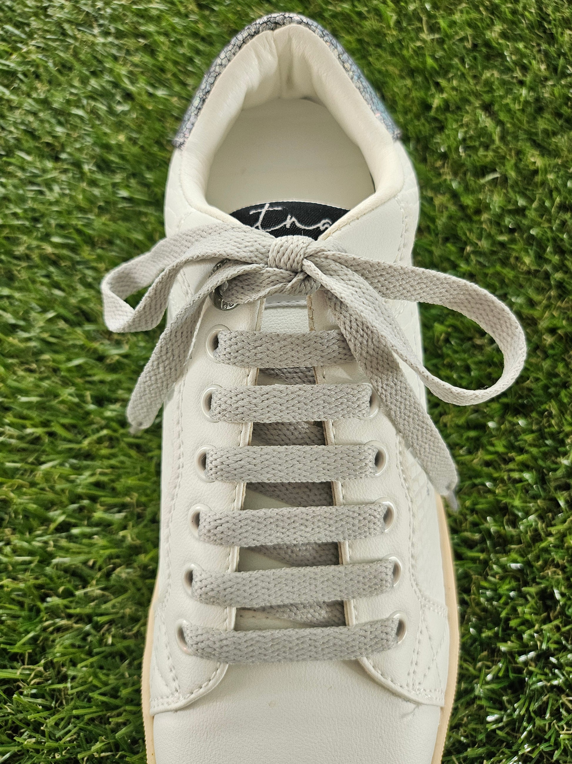 White sneaker with gray laces on a grass background