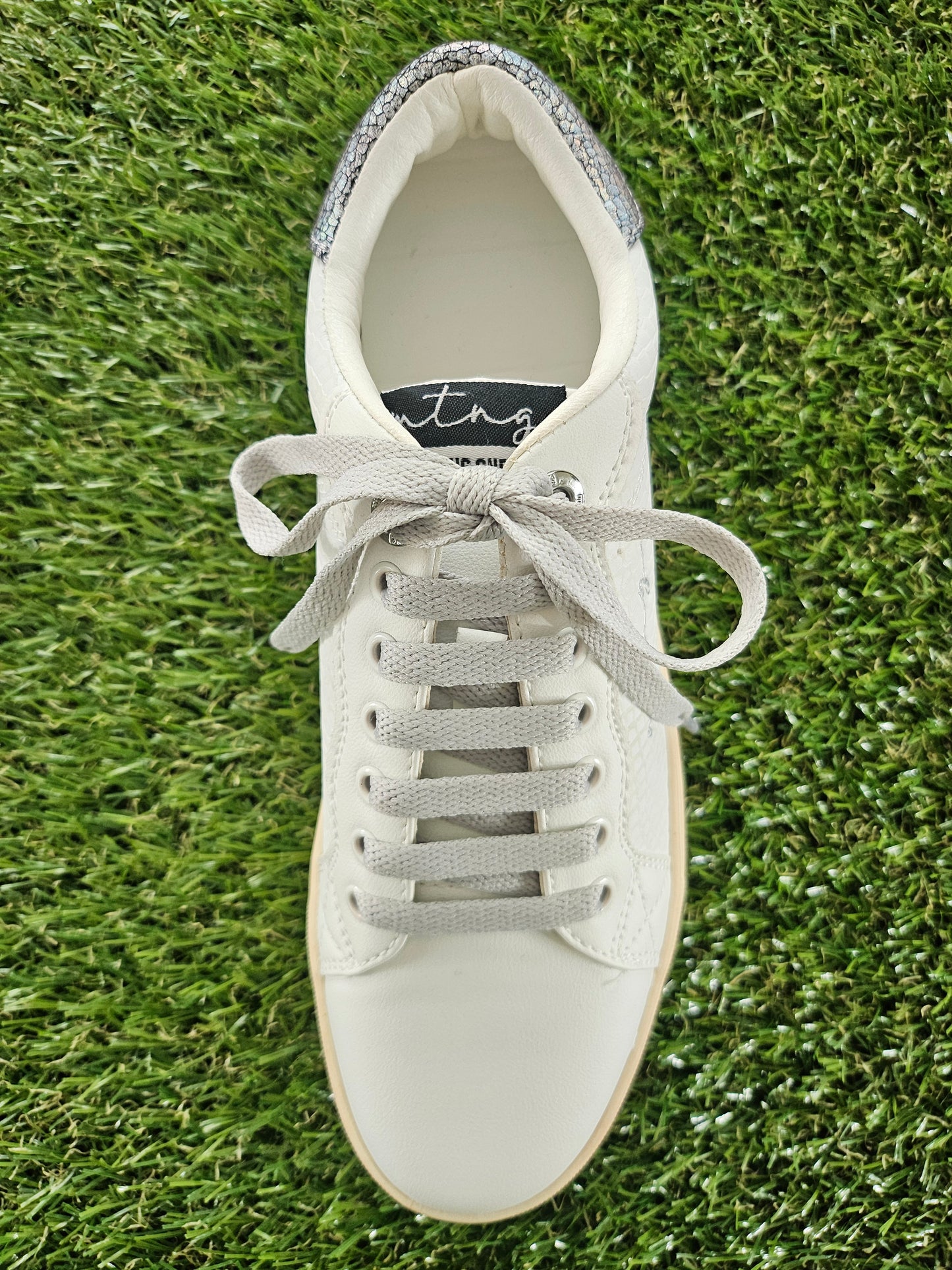 White sneaker with gray laces on a grass background