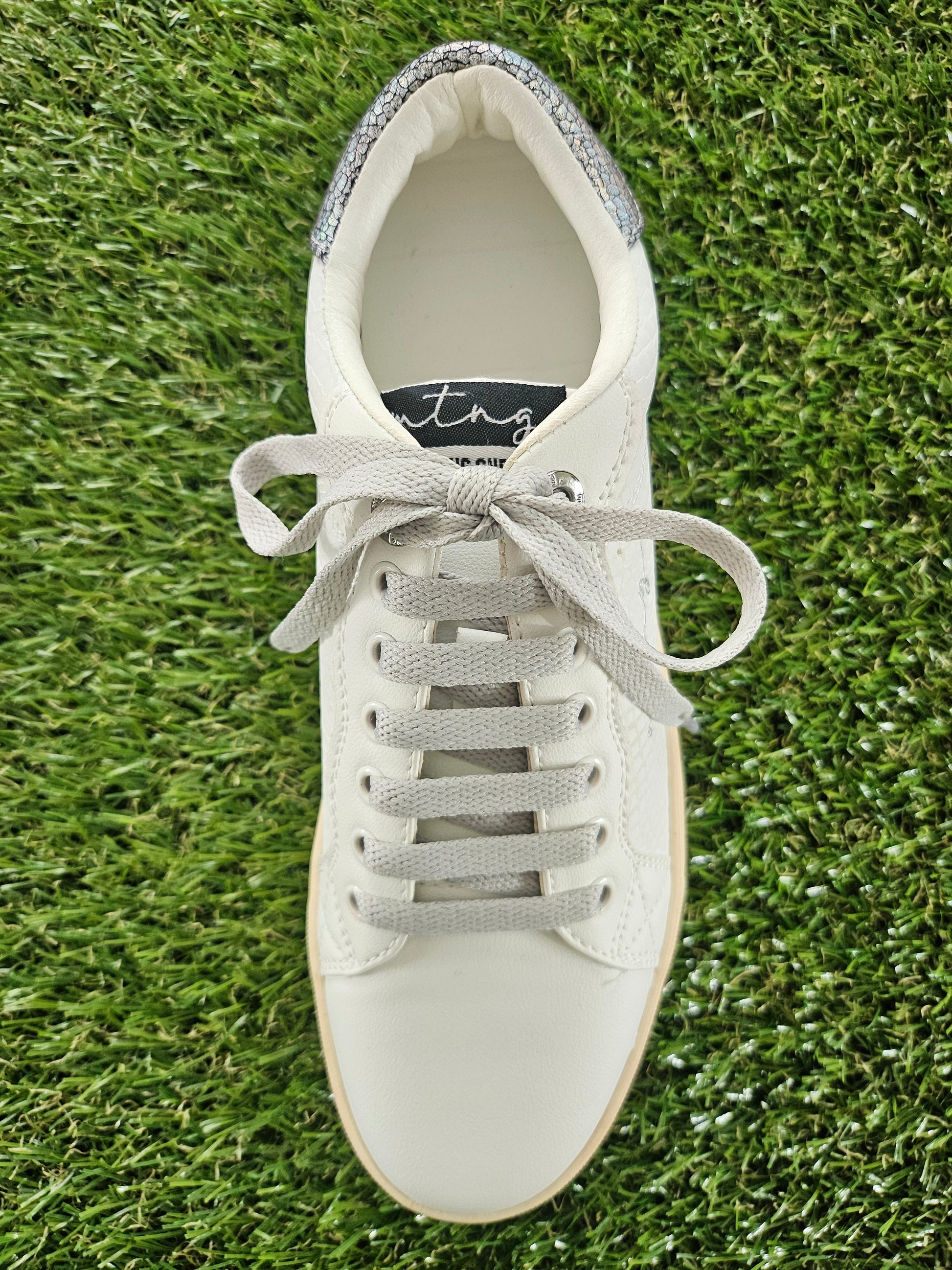 White sneaker with gray laces on a grass background