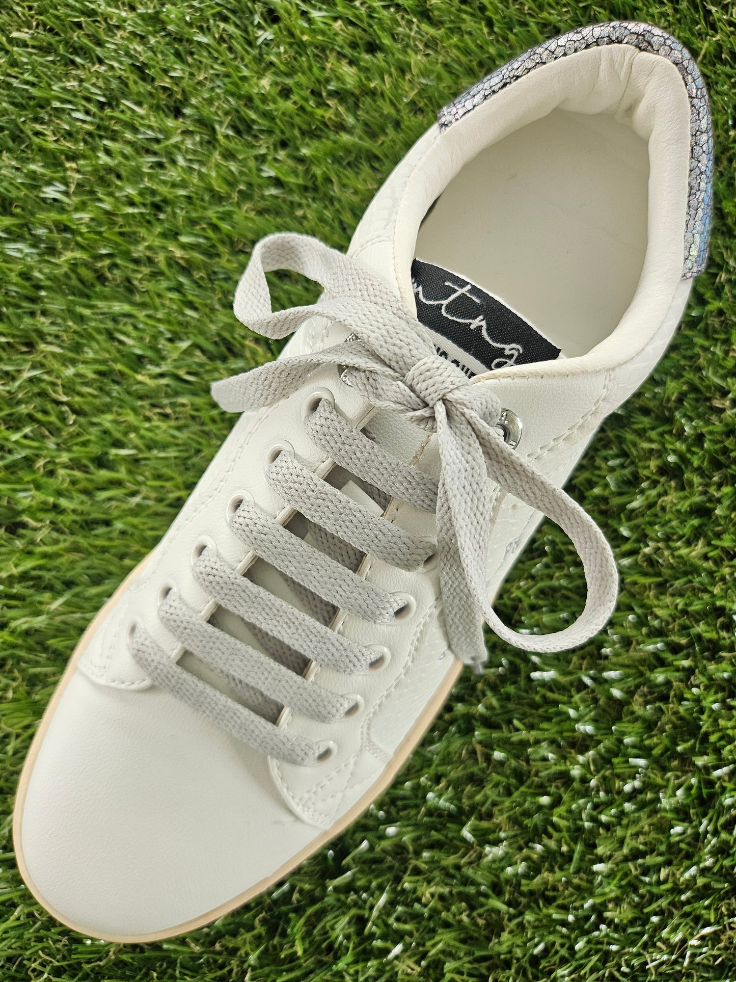 White sneaker with gray laces on grass