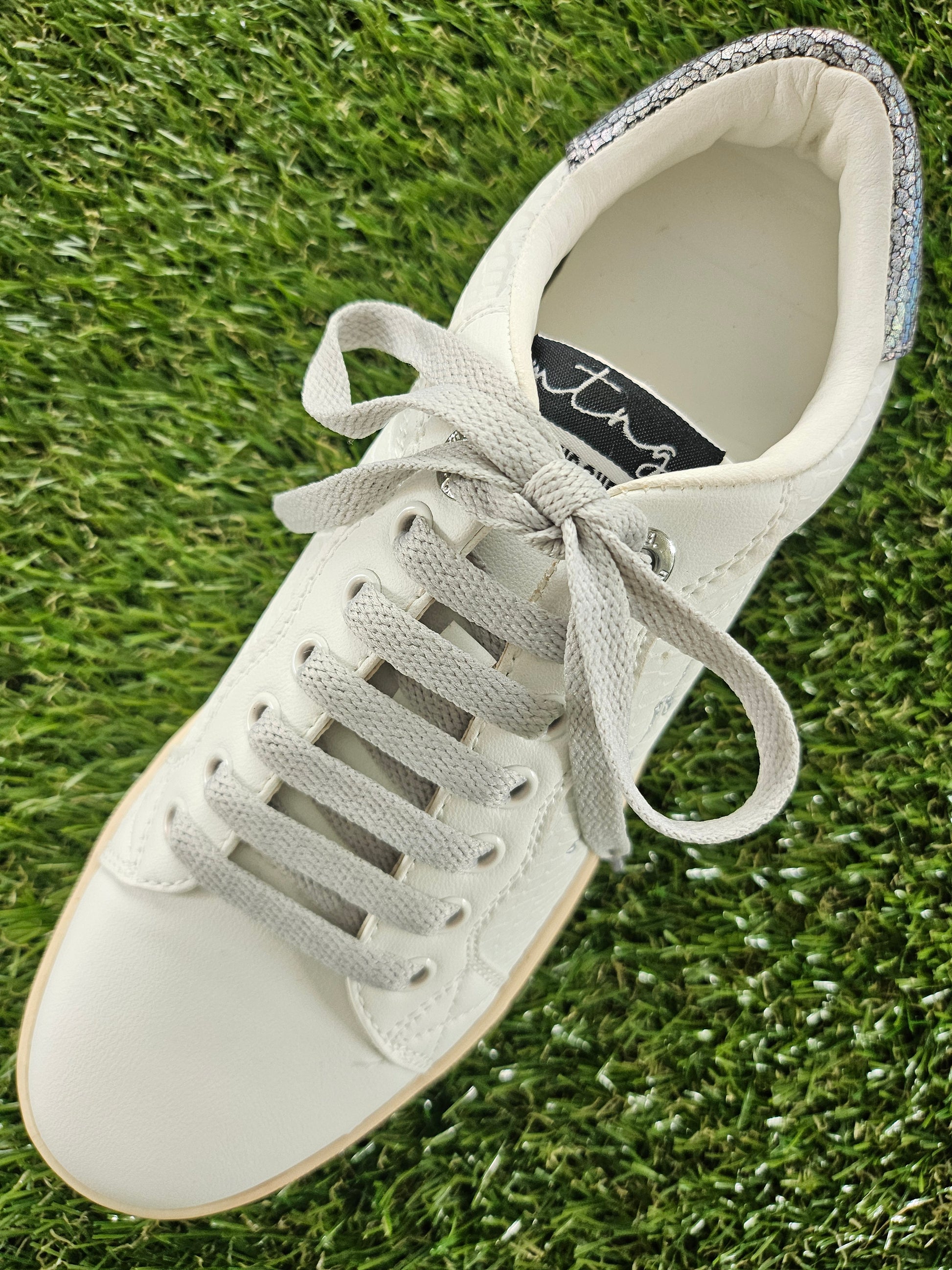White sneaker with gray laces on grass