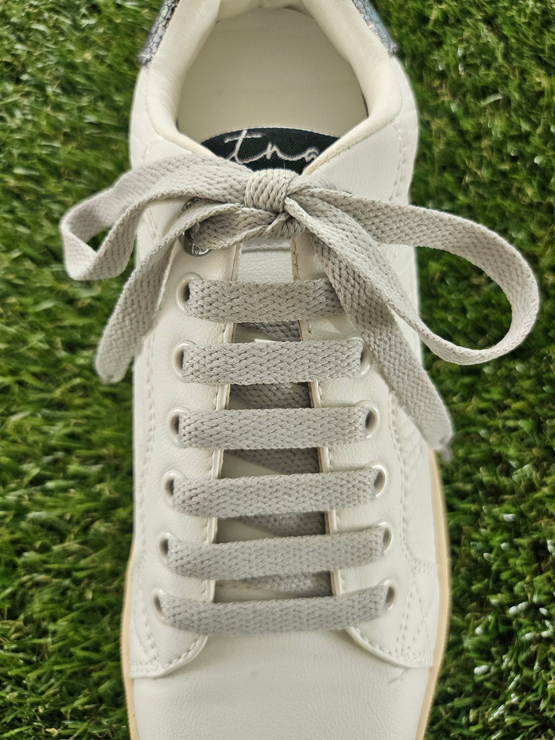 White sneaker with gray laces on a grass background