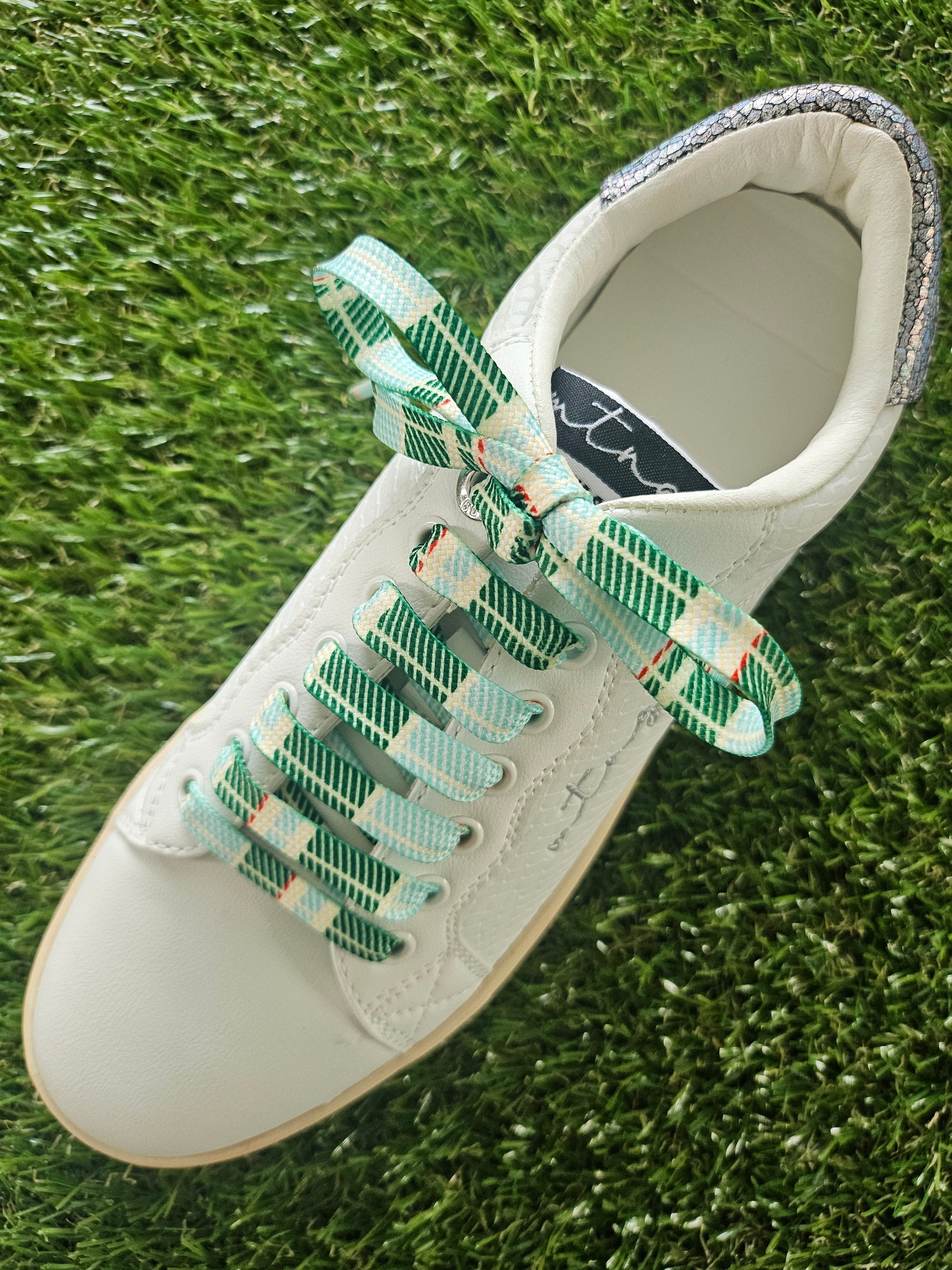 White shoe with green tartan plaid laces on grass