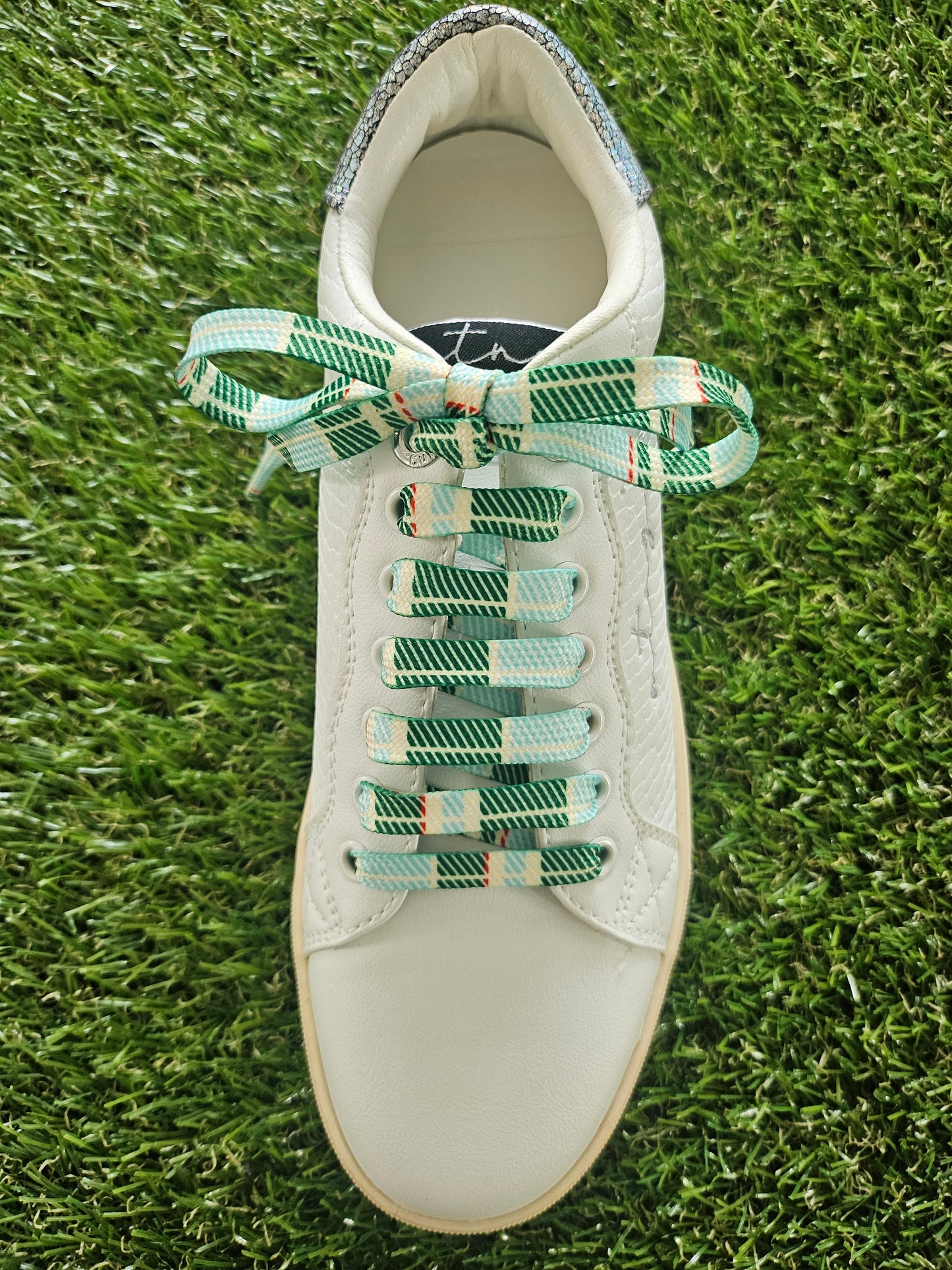 White sneaker with green and multicolor laces on grass